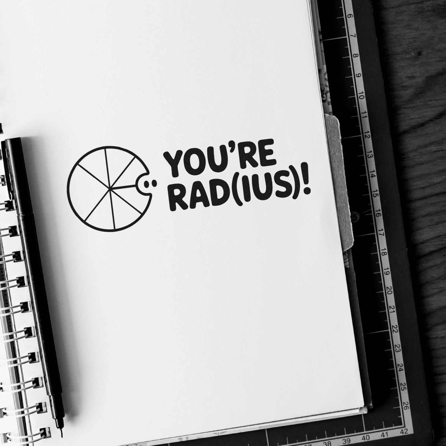 Black-and-white stamp and seal design with a circular seal icon and bold YOURE RAD(IUS)! text on a notebook.