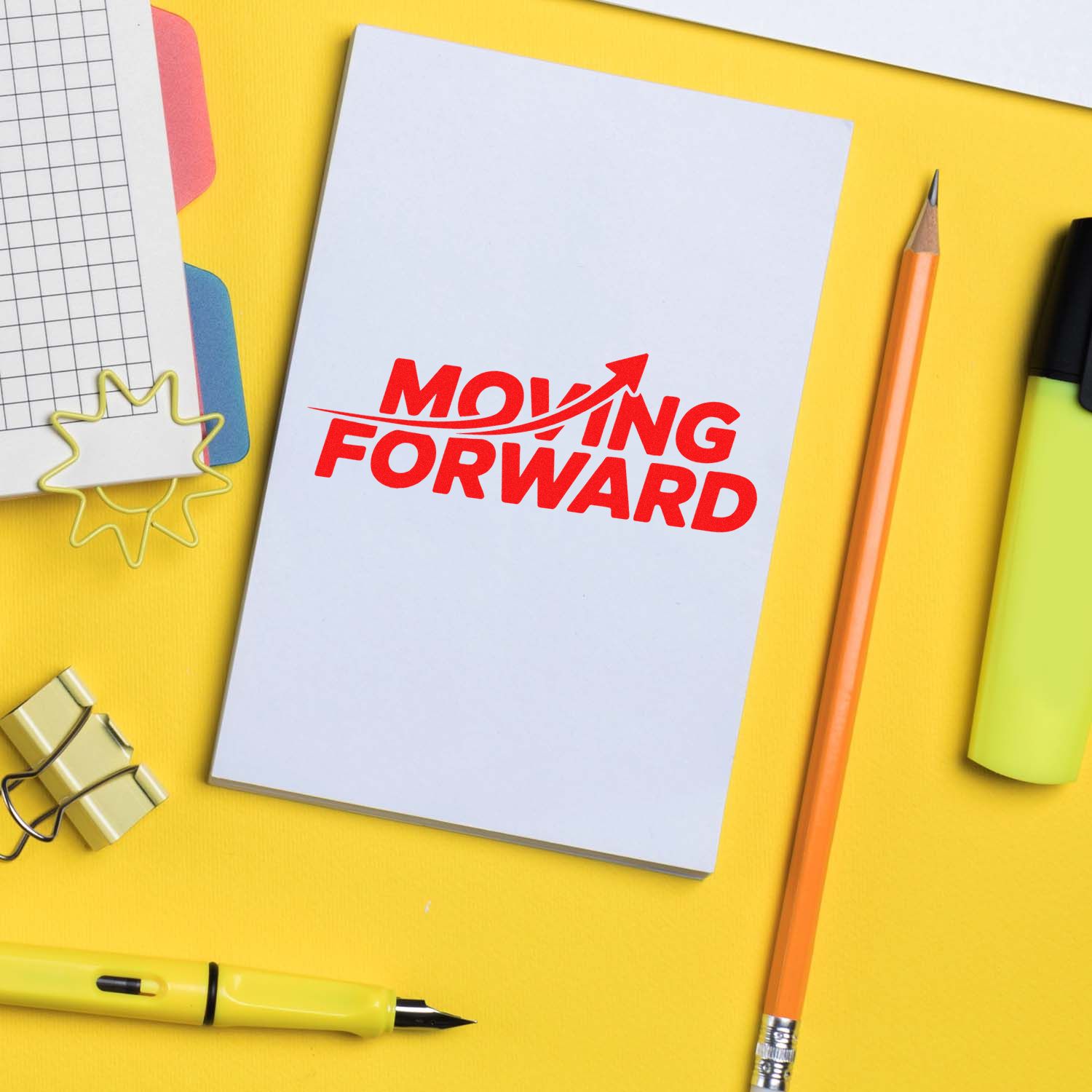 White notebook with red Moving Forward stamp, yellow desk, pencil, and office stamp and seal supplies.
