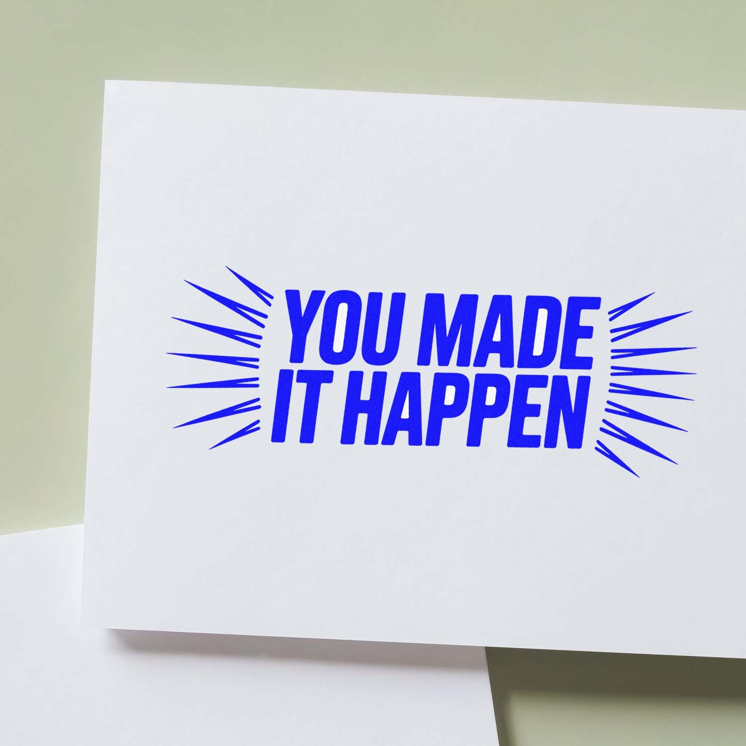 Blue YOU MADE IT HAPPEN stamp seal on white card with burst lines, against a pale green background.