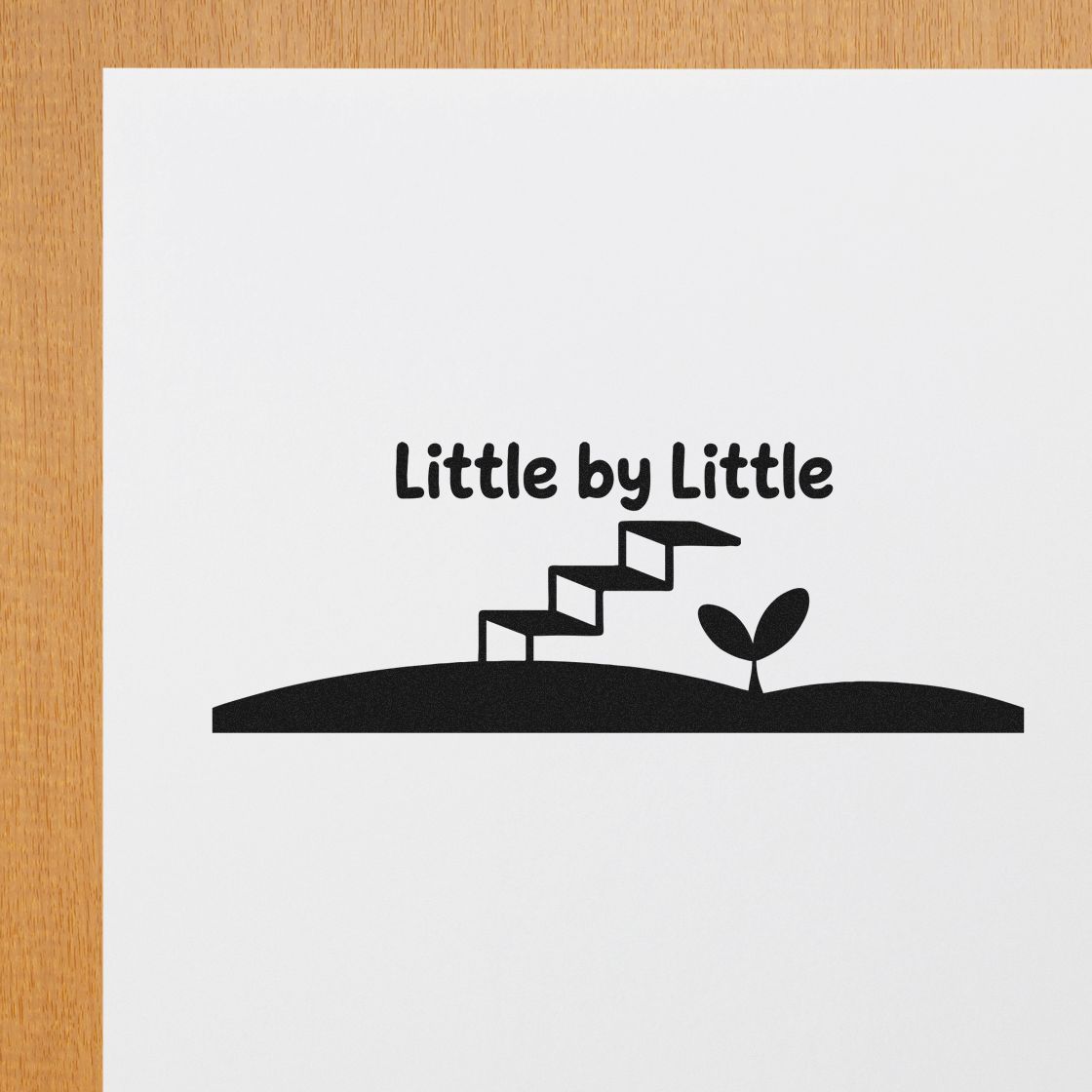 Black stamp seal reading Little by Little with stepping stones and sprout on white paper over a wood background.