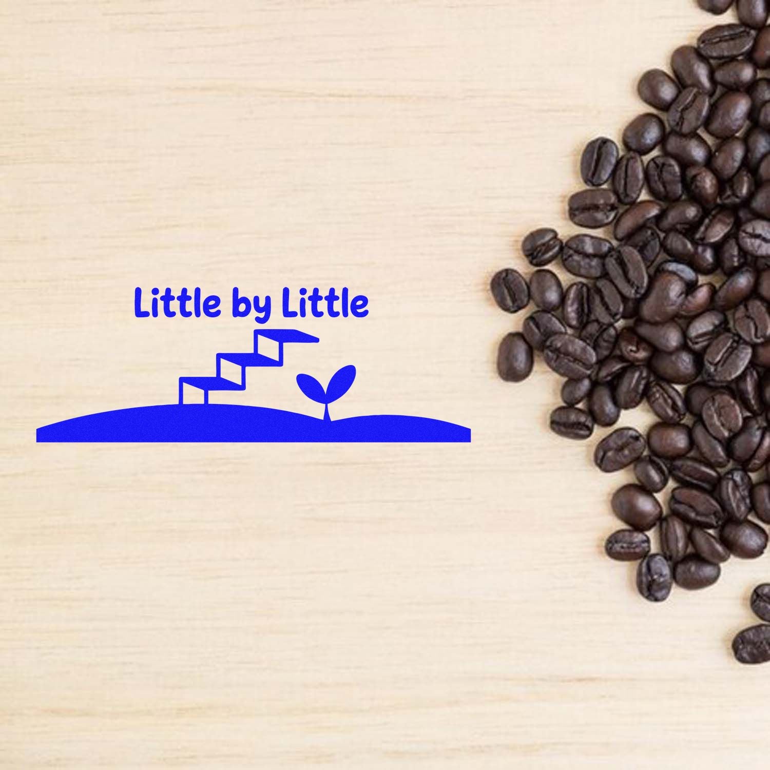 Blue Little by Little stamp and seal logo with sprout stairs on light wood, bordered by dark coffee beans.