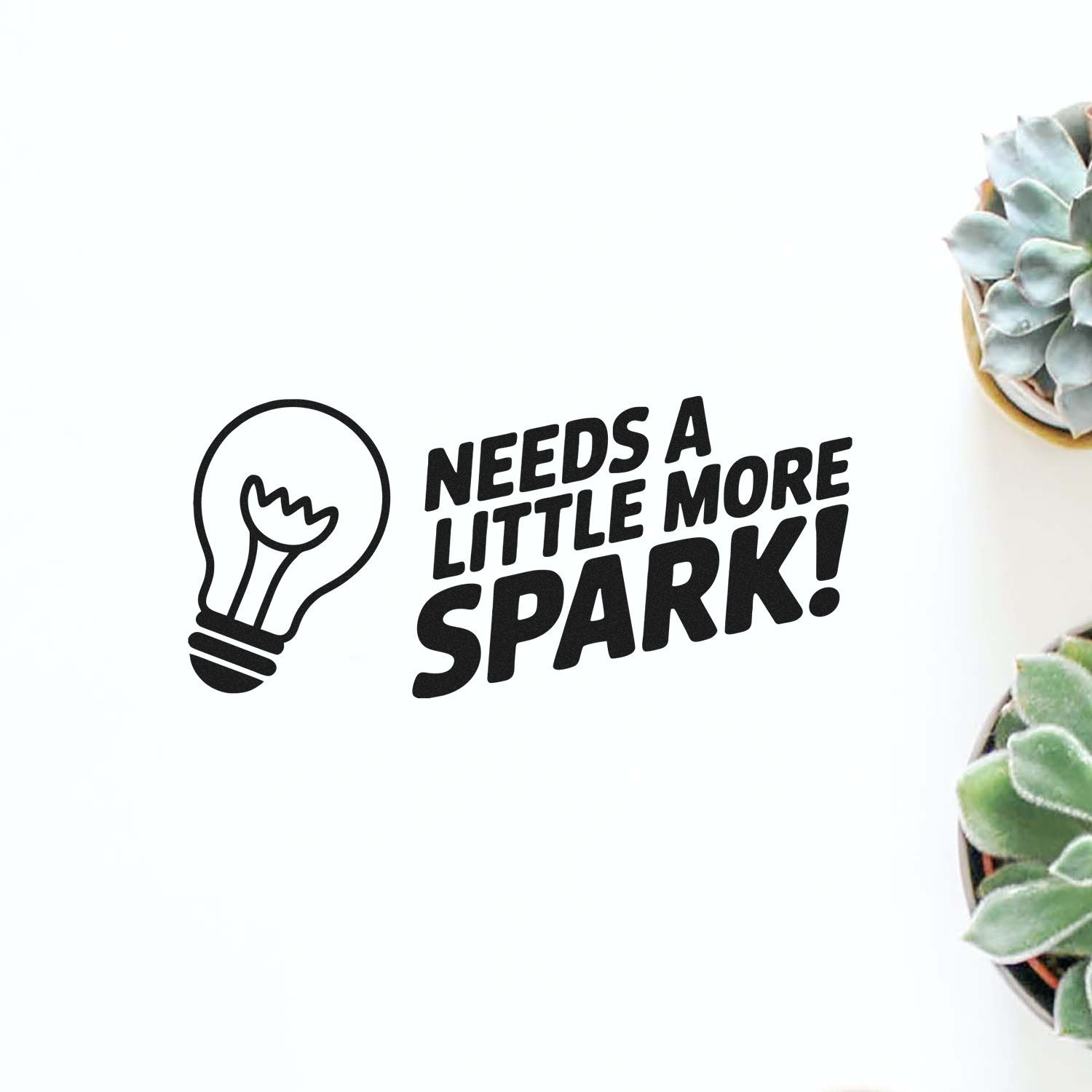 Black stamp seal with lightbulb icon and Needs a little more spark! text on white, with succulents at right.
