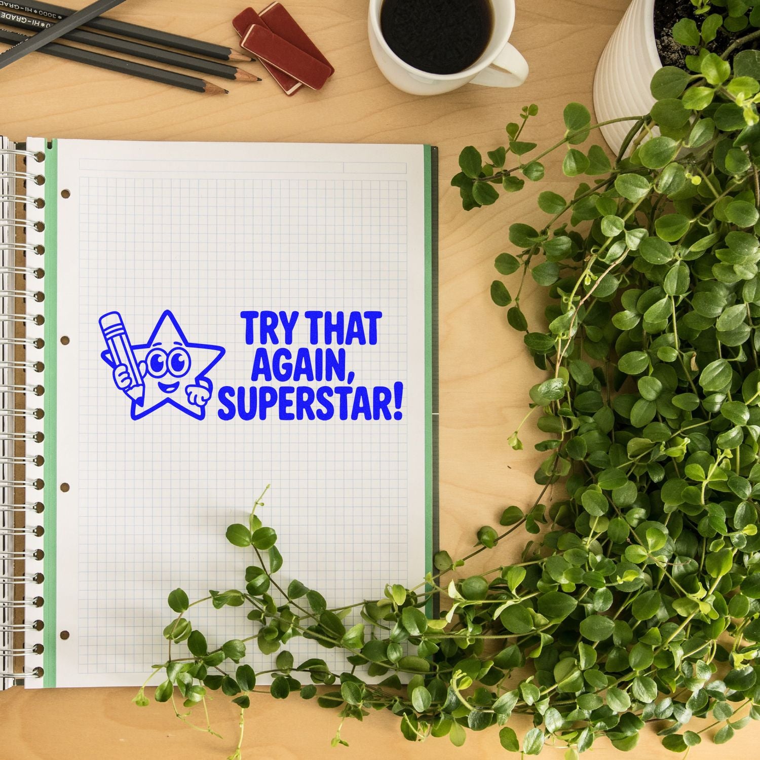 Blue motivational stamp and seal reading Try that again, superstar! on graph notebook, with pencils, coffee, and green plant.