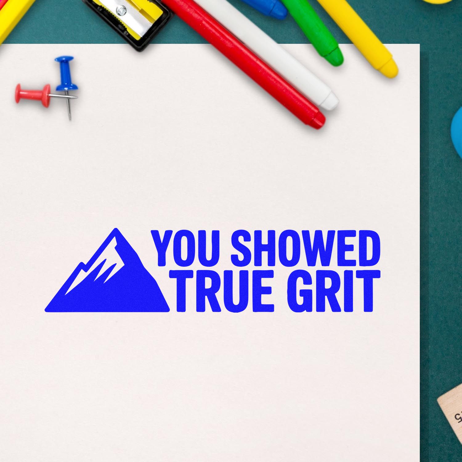 Blue You Showed True Grit stamp and seal on white paper, surrounded by colorful pens and push pins.