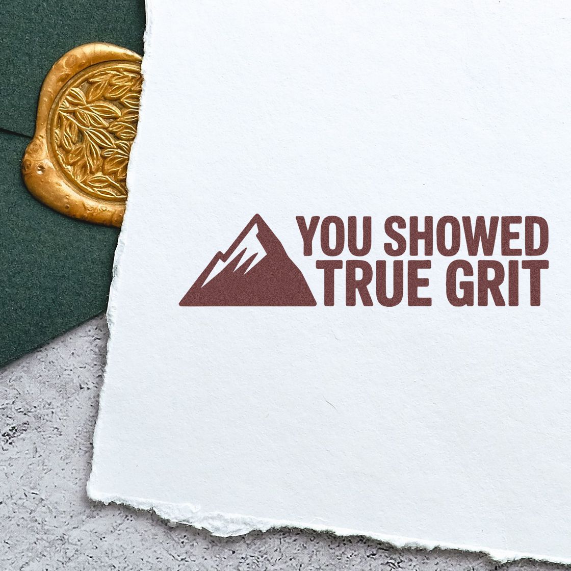 Maroon YOU SHOWED TRUE GRIT stamp on white paper beside a gold embossed seal on dark green background.
