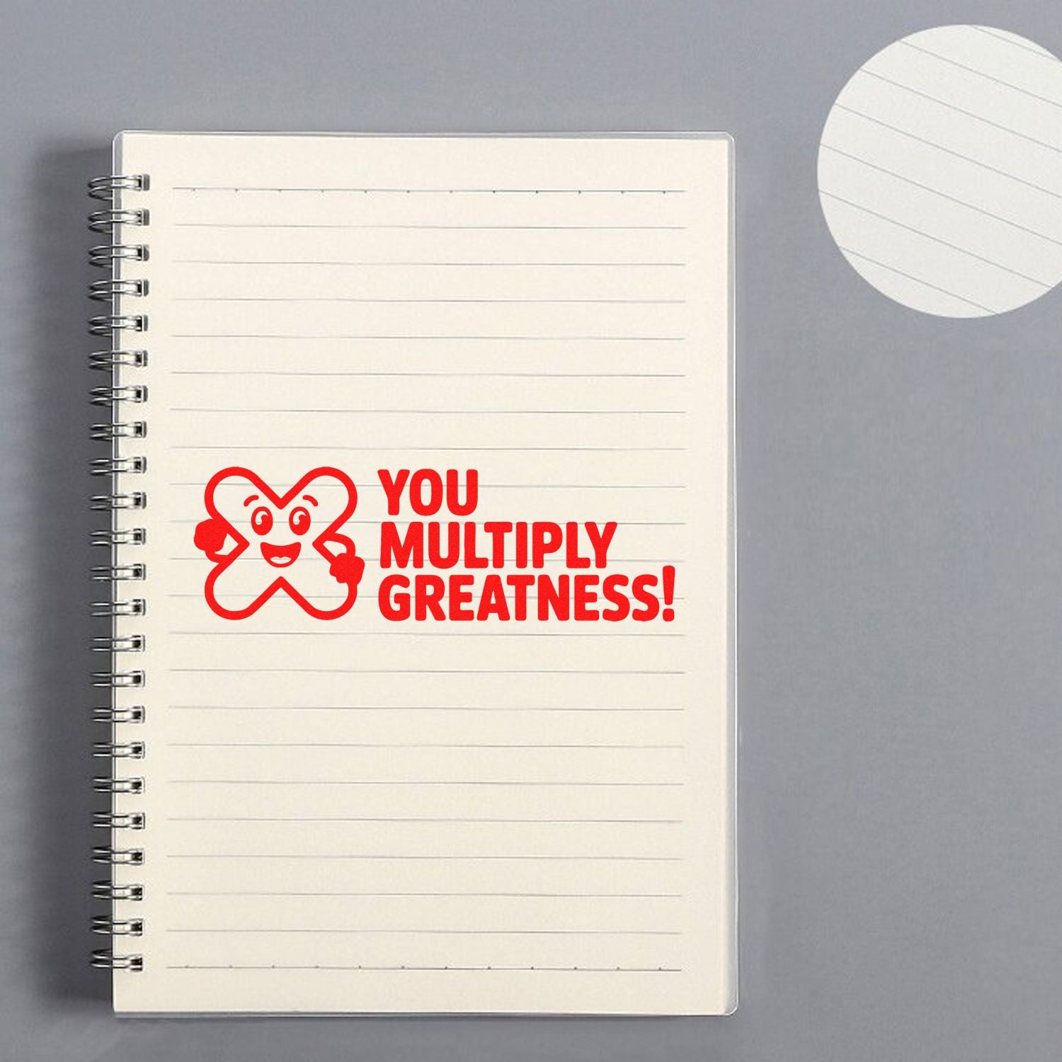 Red stamp seal reading You Multiply Greatness! on a cream lined spiral notebook.