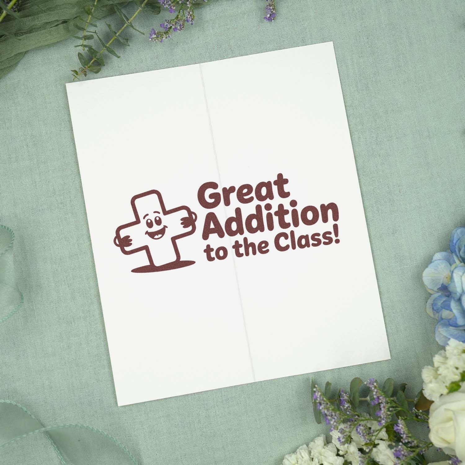 Brown classroom stamp seal reading Great Addition to the Class! with smiling cross on white card.
