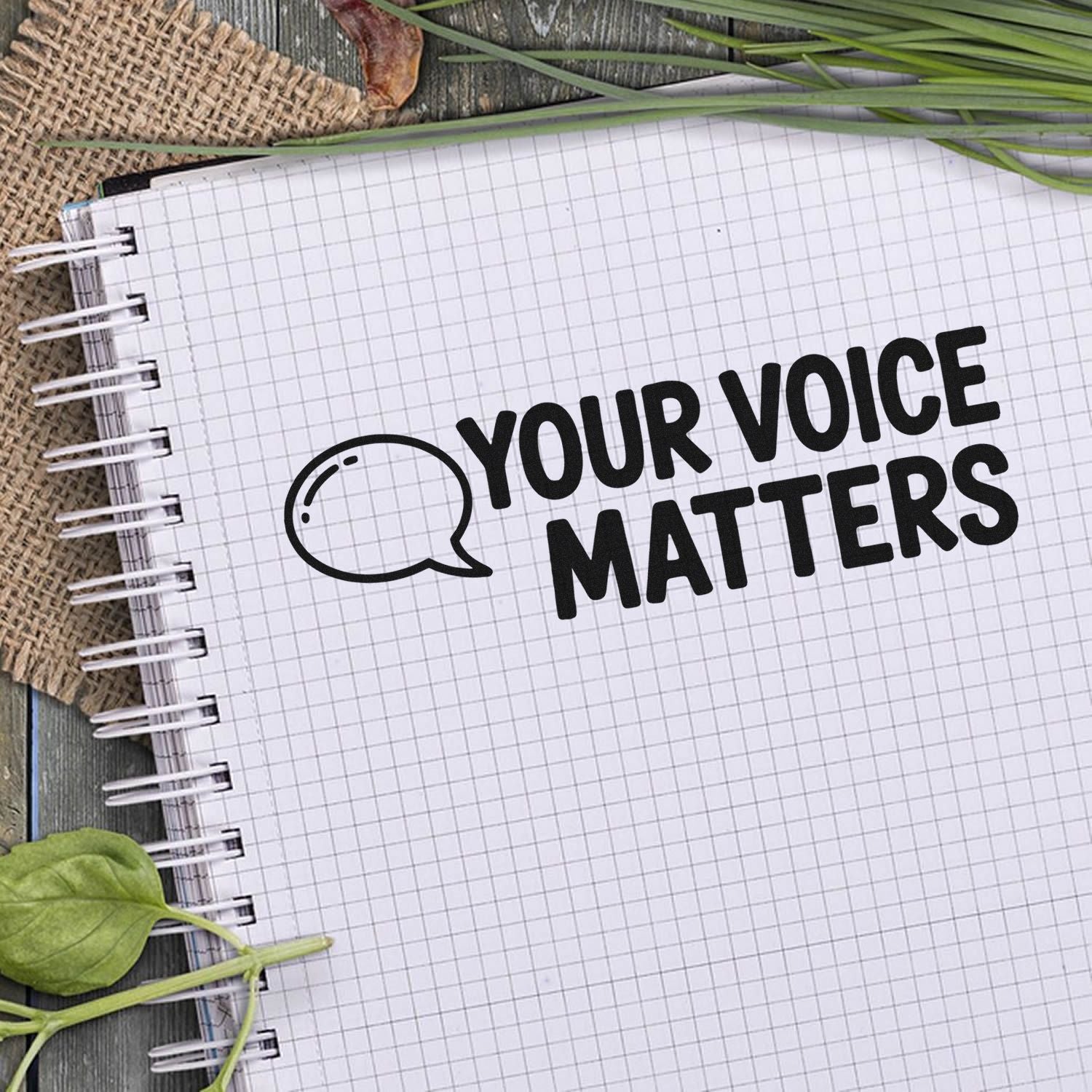 Black custom stamp and seal logo on white grid notebook reading Your Voice Matters, with speech bubble icon and green leaves.