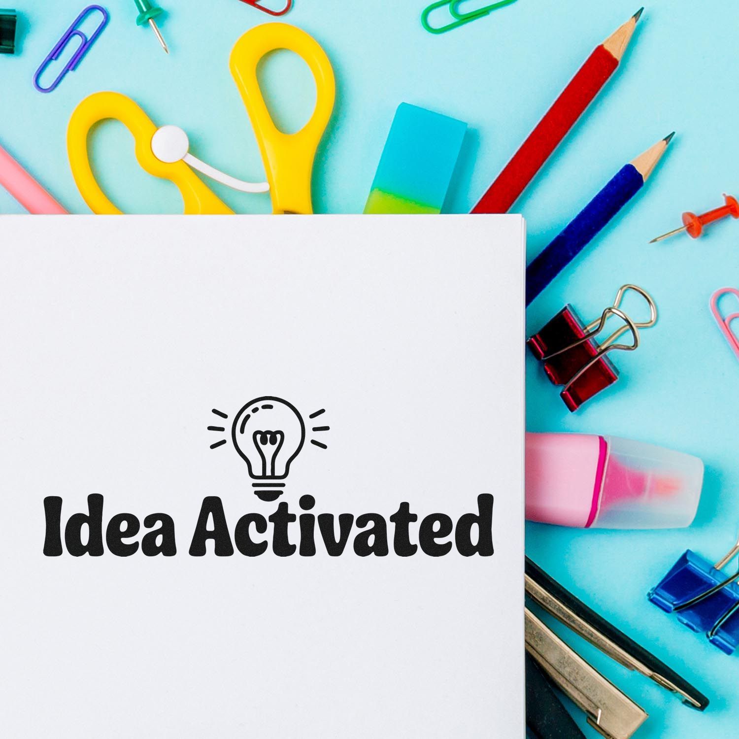 White Idea Activated stamp and seal card with lightbulb, surrounded by colorful stationery on a blue background.