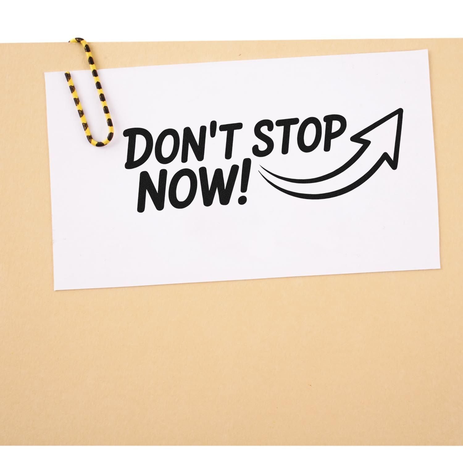 Black Dont Stop Now! stamp and seal with arrow on white card, clipped by a yellow-black paperclip on beige background.