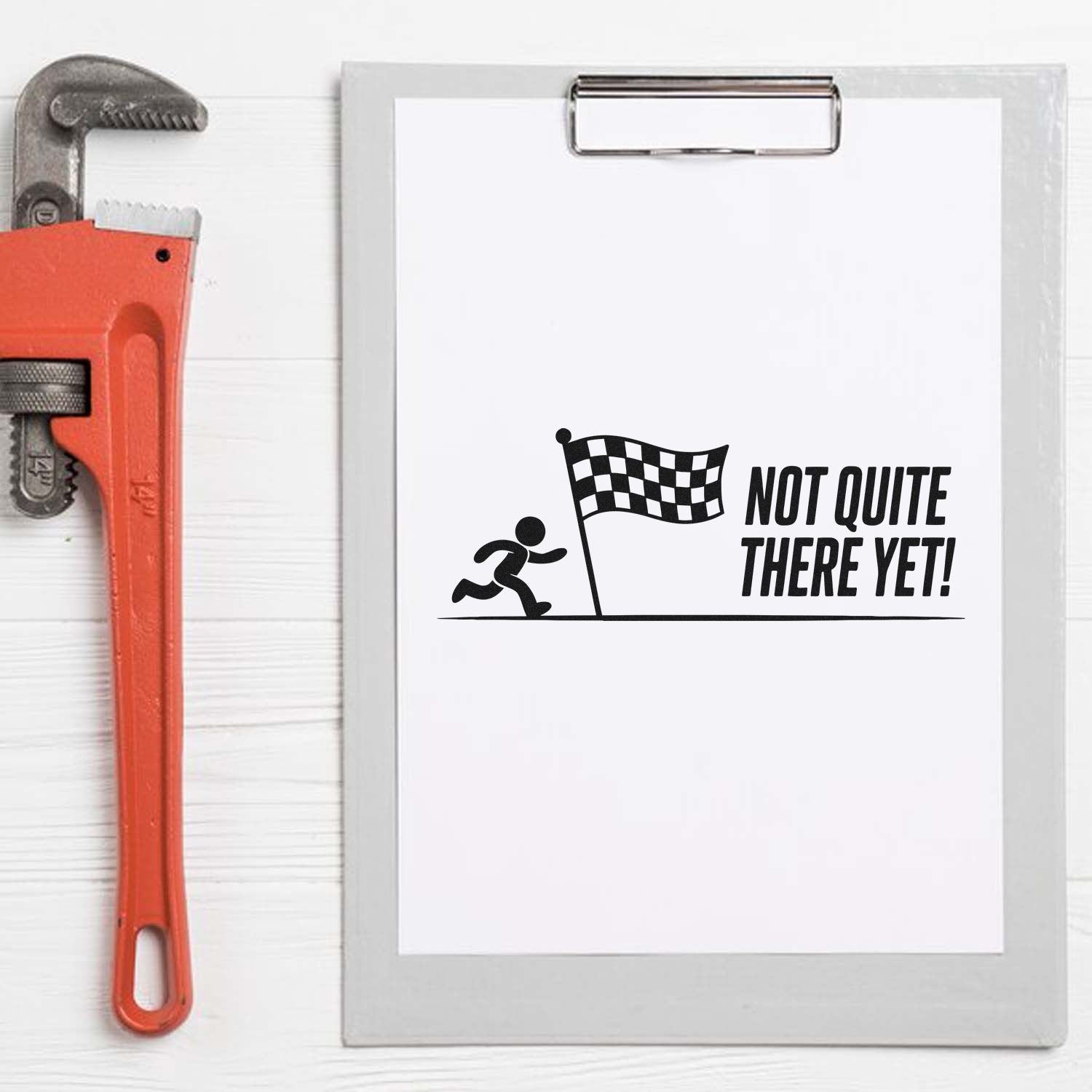 Orange pipe wrench stamp and silver clipboard with black checkered-flag Not Quite There Yet! seal design