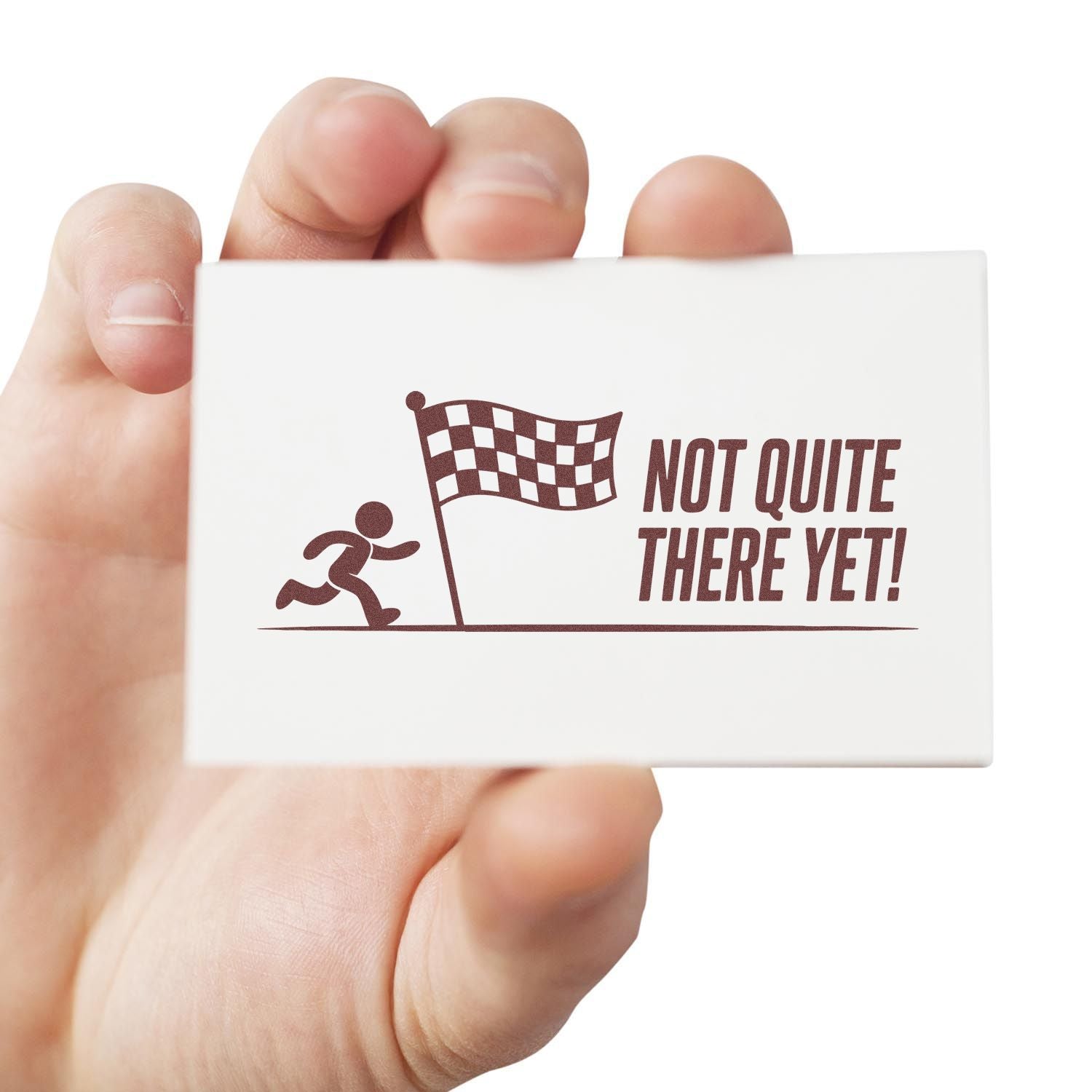White rubber stamp seal with brown runner and checkered flag graphic and Not Quite There Yet! text in a hand.