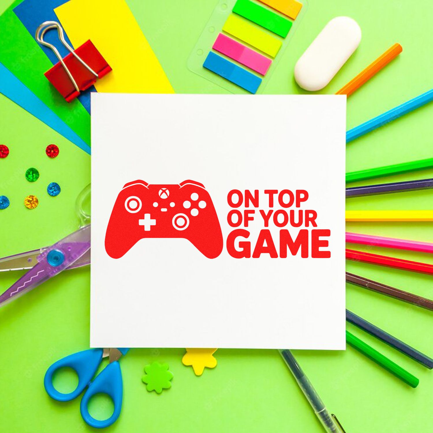 Red game controller stamp seal on white card, surrounded by neon stationery on green background