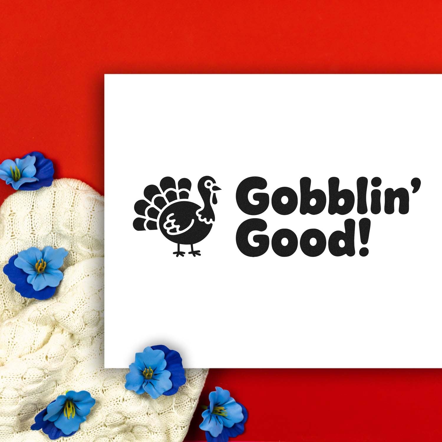Black turkey stamp and seal design with Gobblin Good! on white card, set on red background with cream knit and blue flowers.