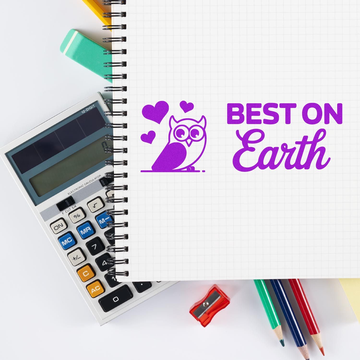 Purple owl seal stamp with hearts and Best on Earth on a grid notebook, beside a calculator, pencils, and sharpener.