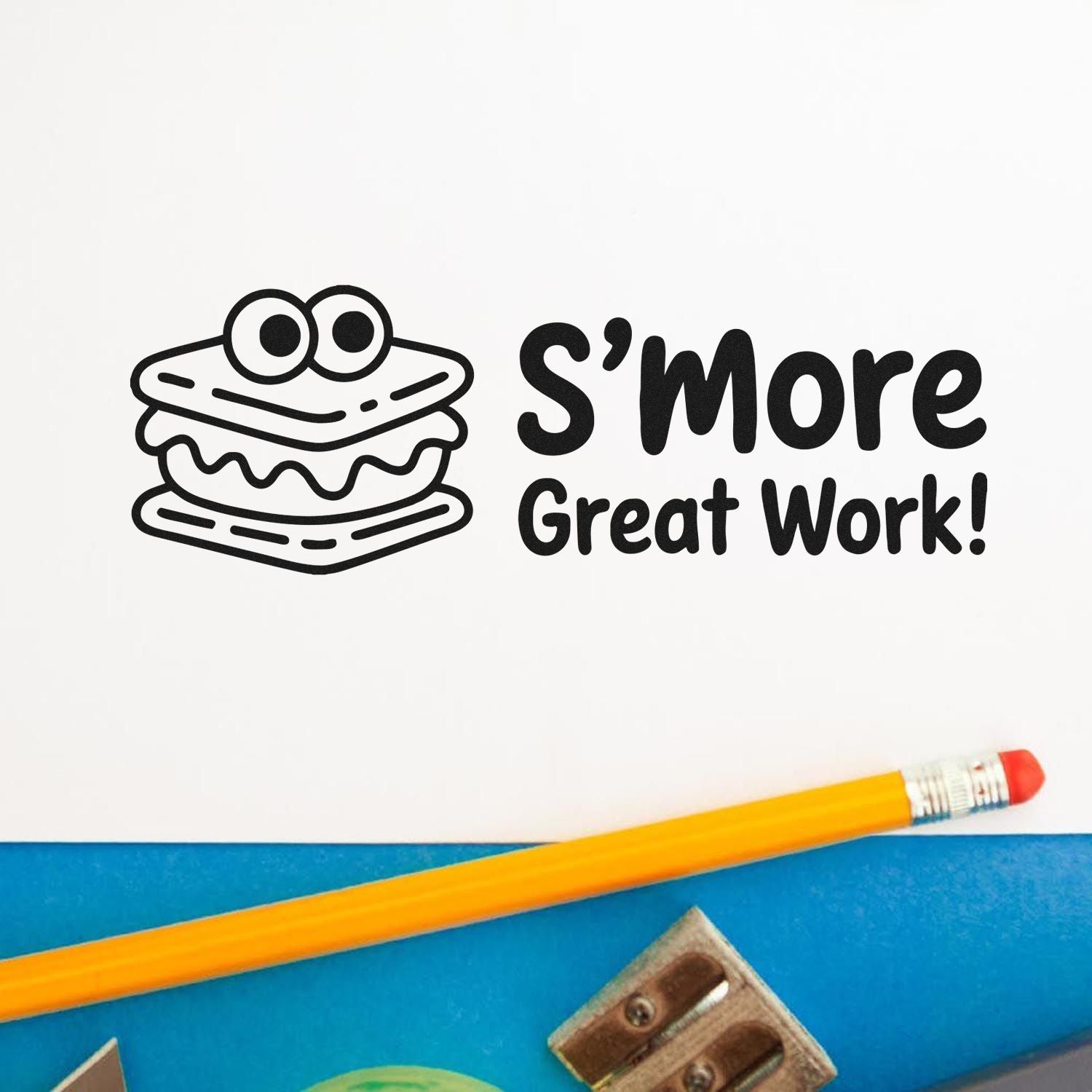 Black S'more Great Work! stamp and seal with cartoon s'more, on white paper beside a yellow pencil and blue background.