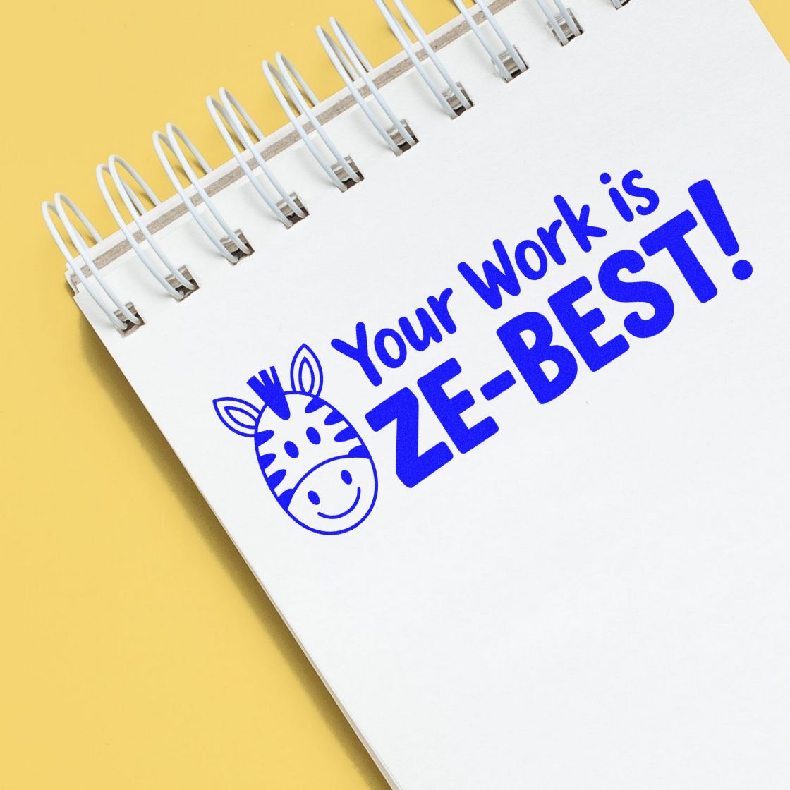 Blue zebra stamp seal on white spiral notebook with Your Work is ZE-BEST! in blue on a yellow background.