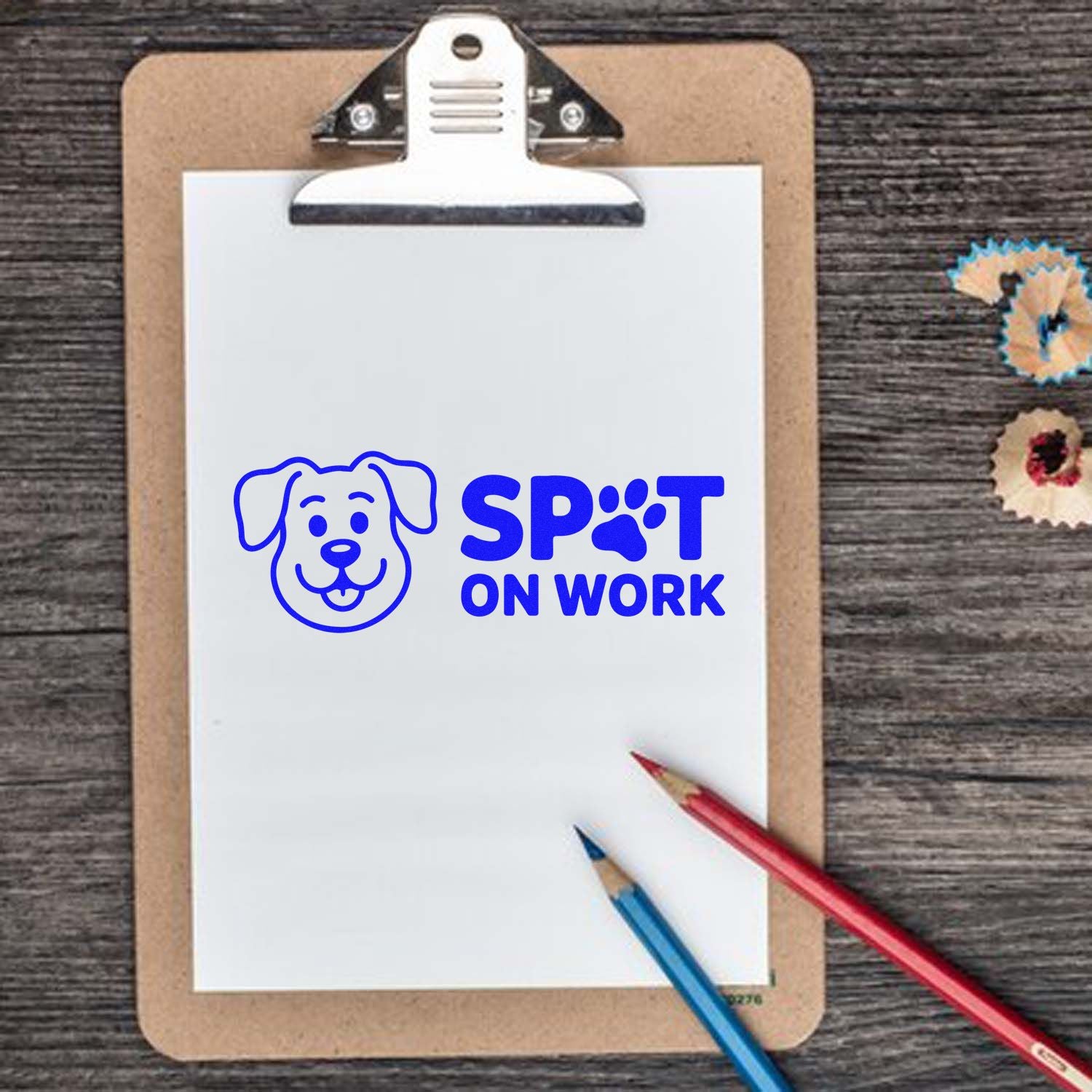 Blue dog logo stamp/seal product reading SPOT ON WORK on a clipboard, with red and blue pencils on wood.