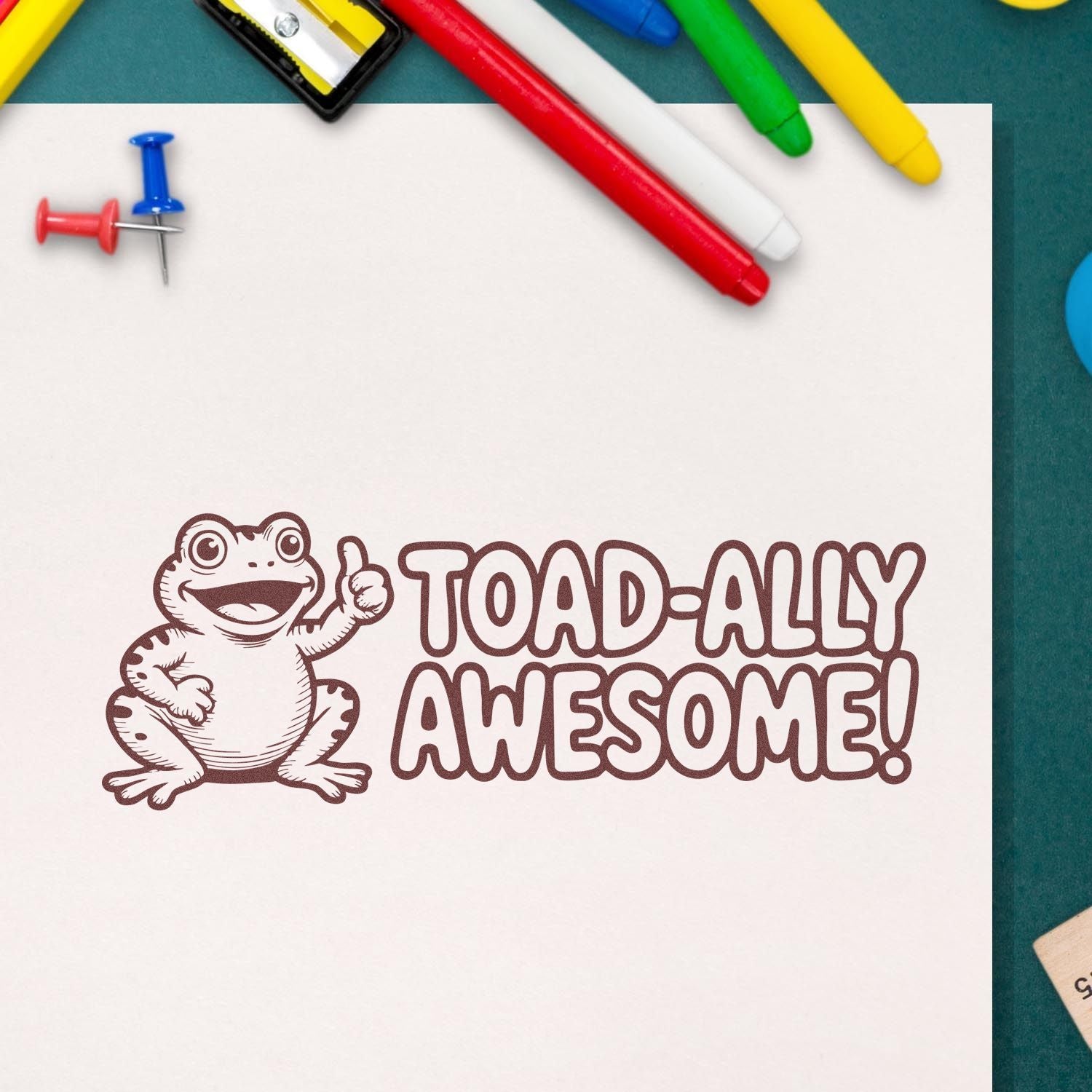Brown frog TOAD-ALLY AWESOME! stamp on white paper, with colorful pens and pushpins around it.