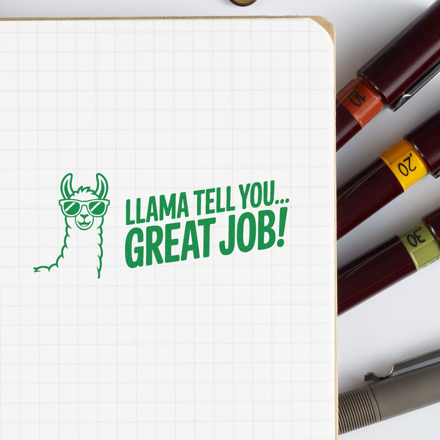 Green llama stamp with Llama tell you... great job! on grid paper, beside burgundy stamp-and-seal markers with orange, yellow, green caps.