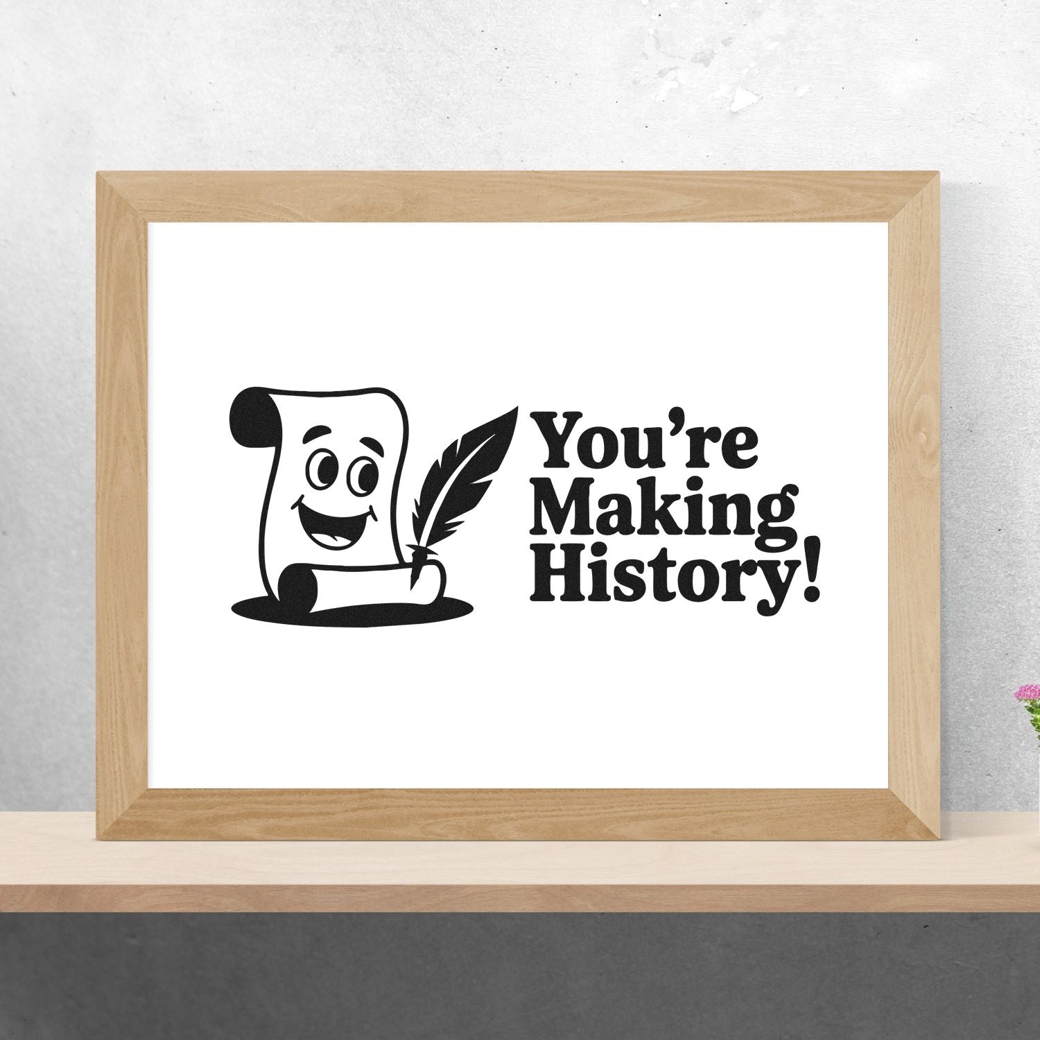 Black stamp and seal design with smiling scroll, quill, and Youre Making History! in a light wood frame.