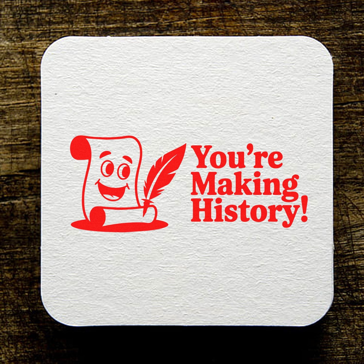 White stamp and seal card with red smiling scroll and quill design, saying Youre Making History! on a dark wood background.
