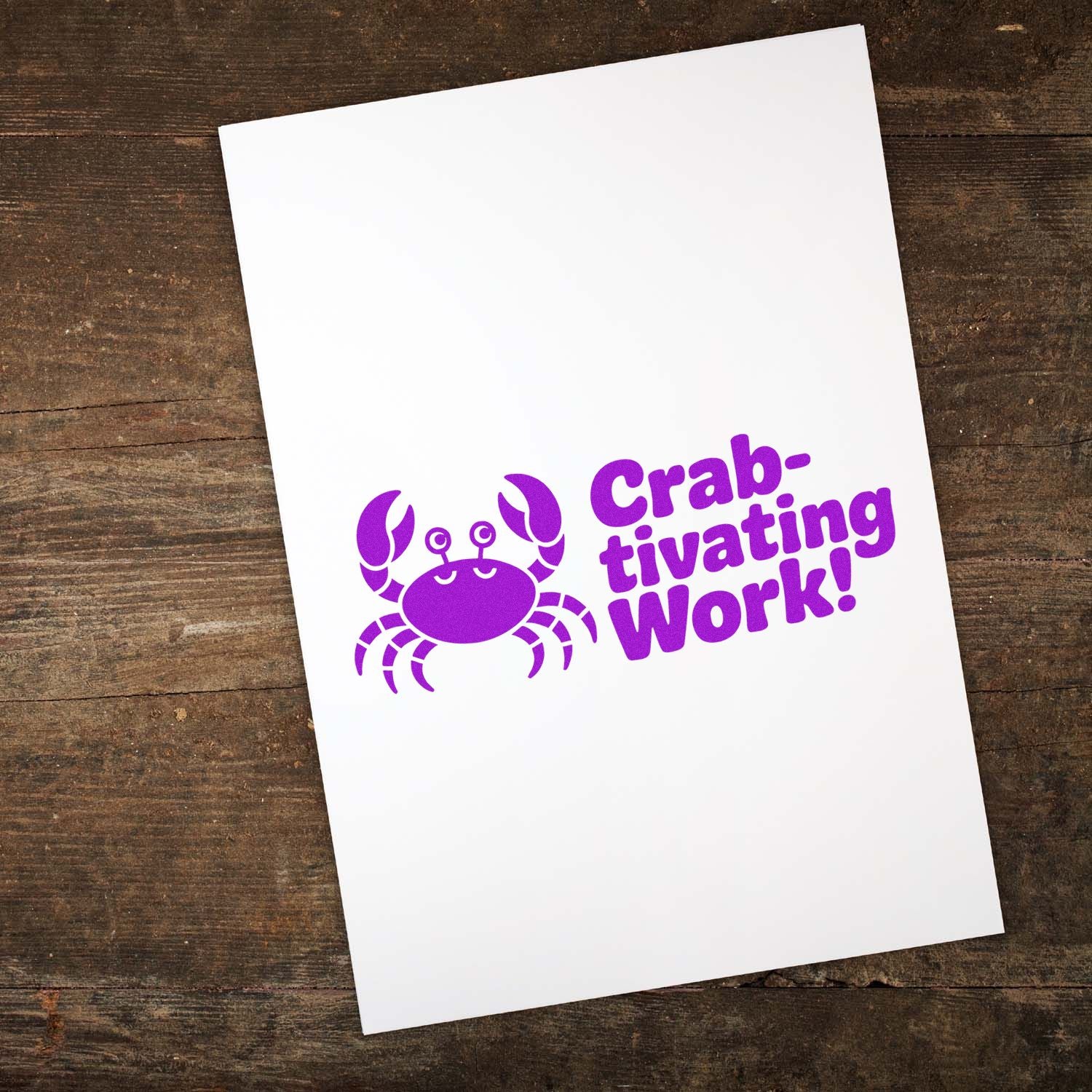 Purple crab stamp seal on white card reading Crab-tivating Work! over a rustic wood background.