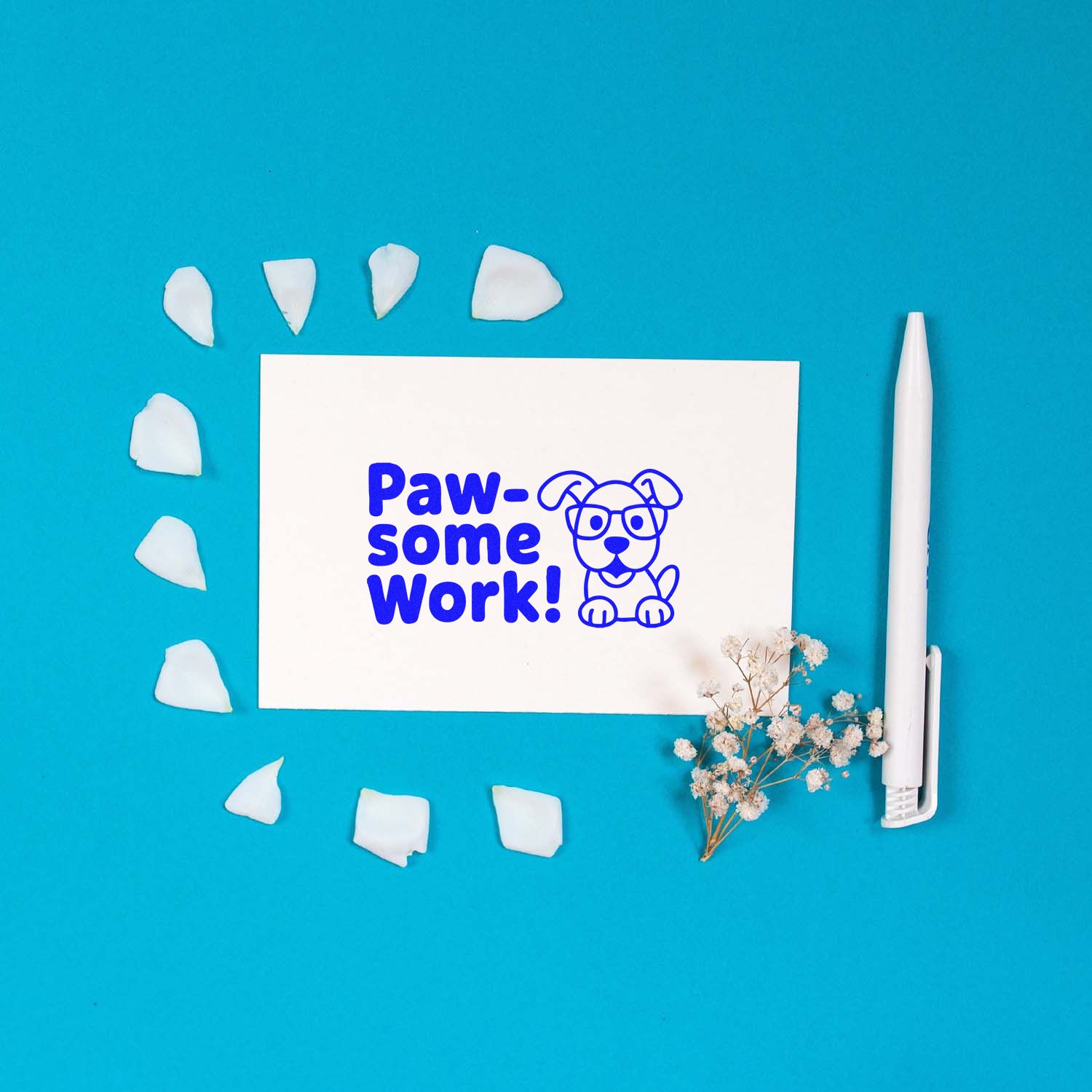 Blue Paw-some Work! dog stamp on white card, with white seal pieces, a white pen, and dried flowers on turquoise background.