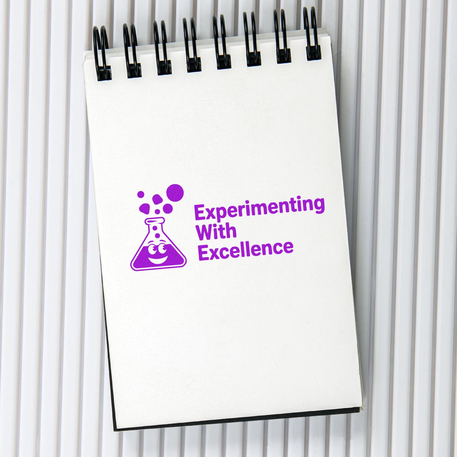White spiral notebook featuring a purple stamp seal logo and Experimenting With Excellence text on a lined background.