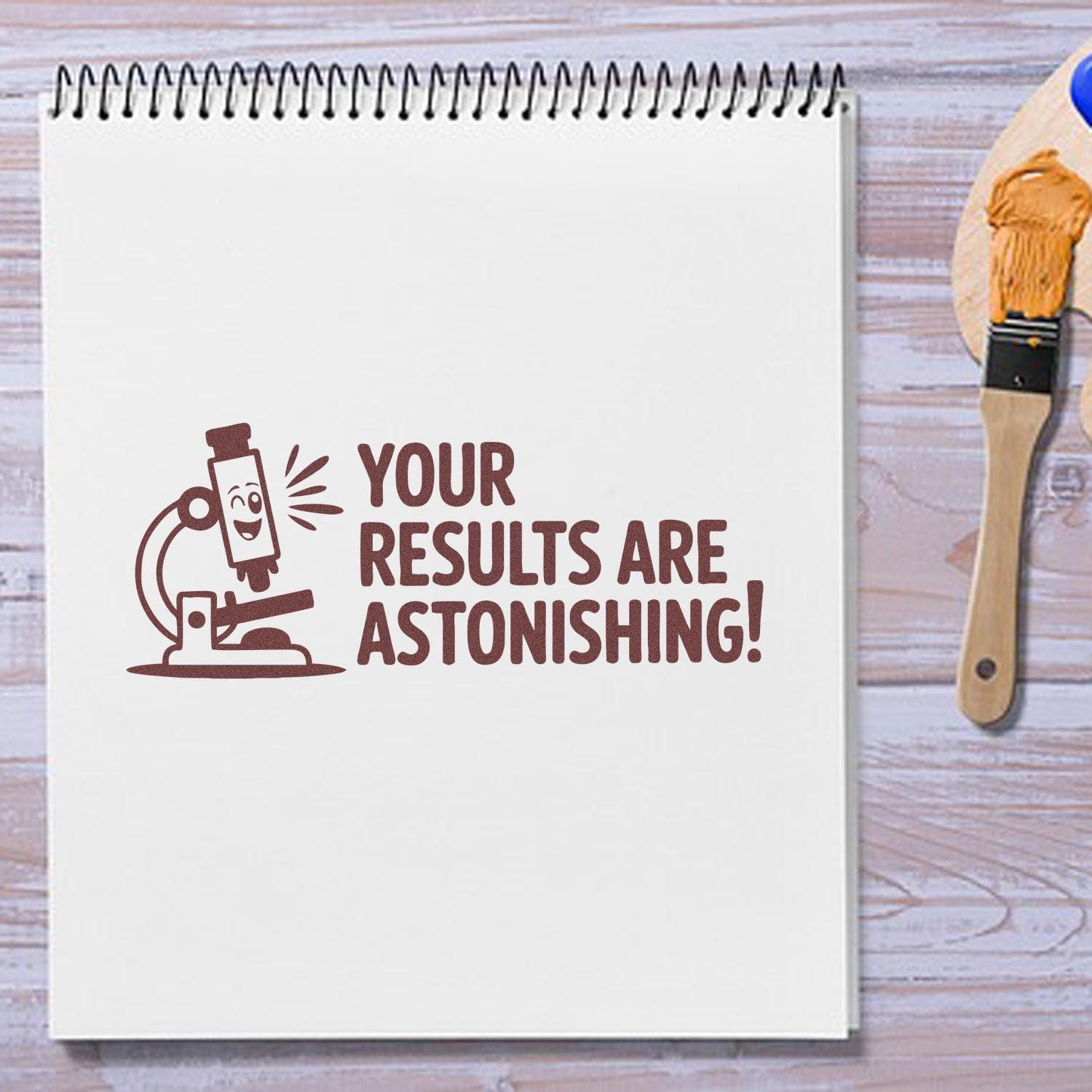 White spiral notebook with brown rubber stamp reading Your Results Are Astonishing! beside a wooden stamp handle.