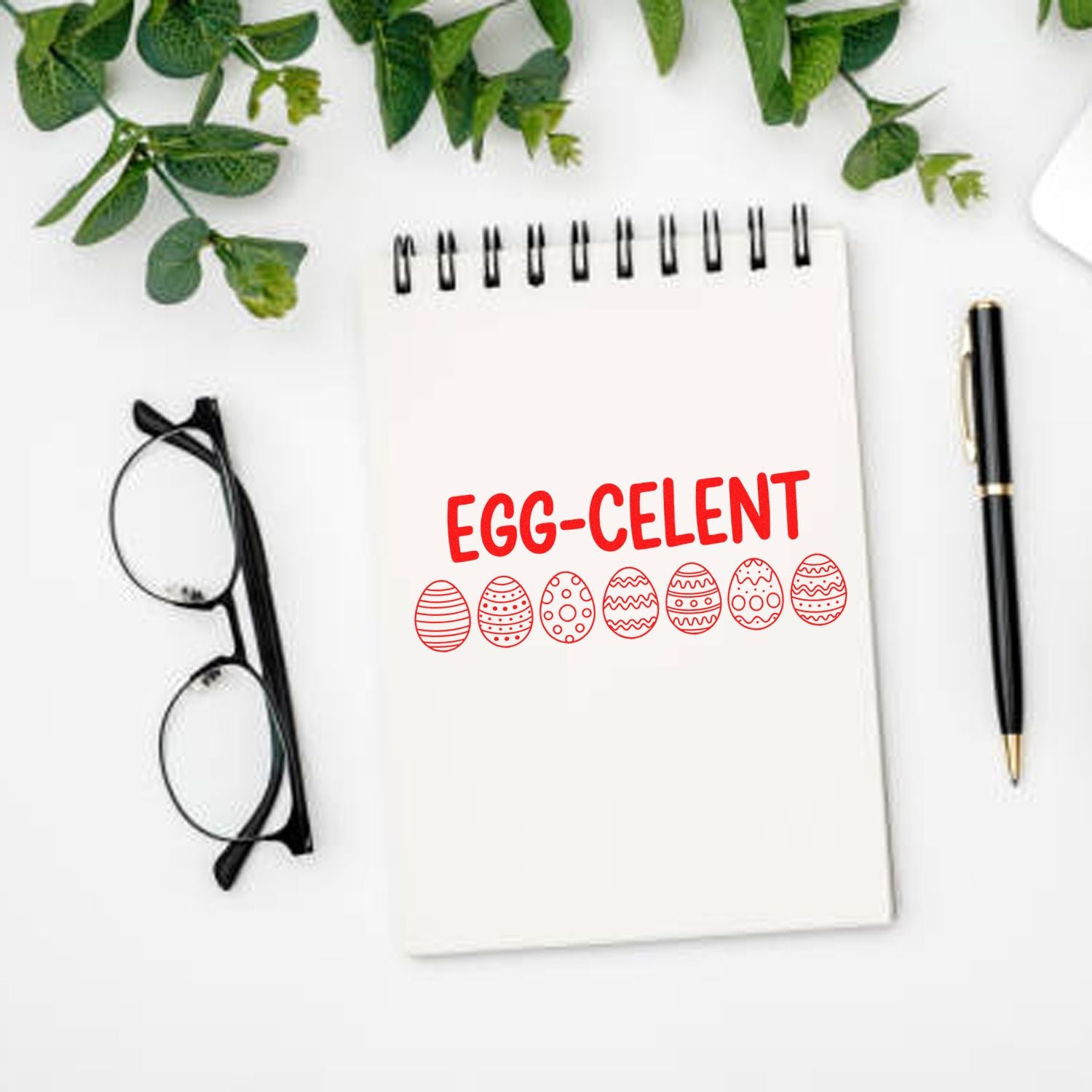 Custom stamp/seal design in red reading EGG-CELENT on white notepad, with egg icons, green leaves, glasses, and black pen.