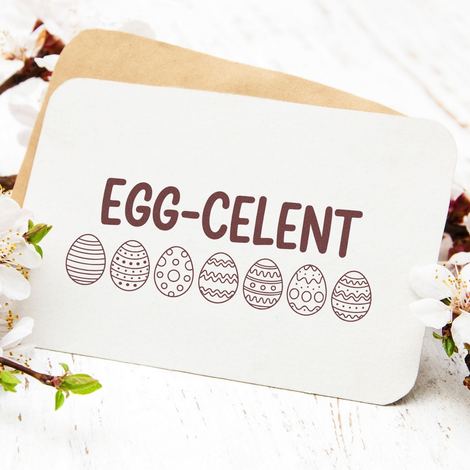 Brown Egg-celent stamp on white card with seven patterned Easter eggs, layered over kraft backing and spring blossoms