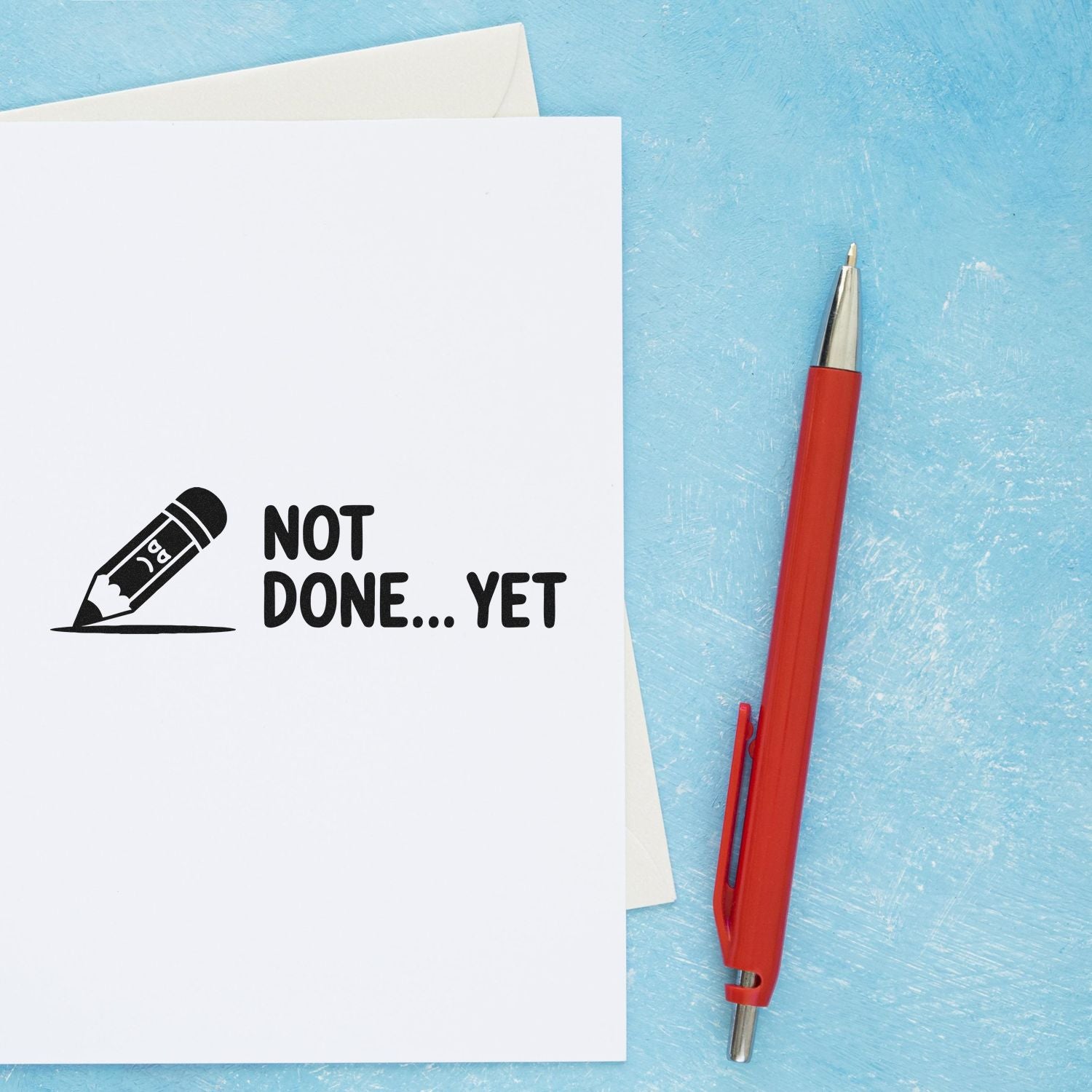 White rubber stamp card reading NOT DONE... YET with pencil icon, beside a red pen on textured blue background.