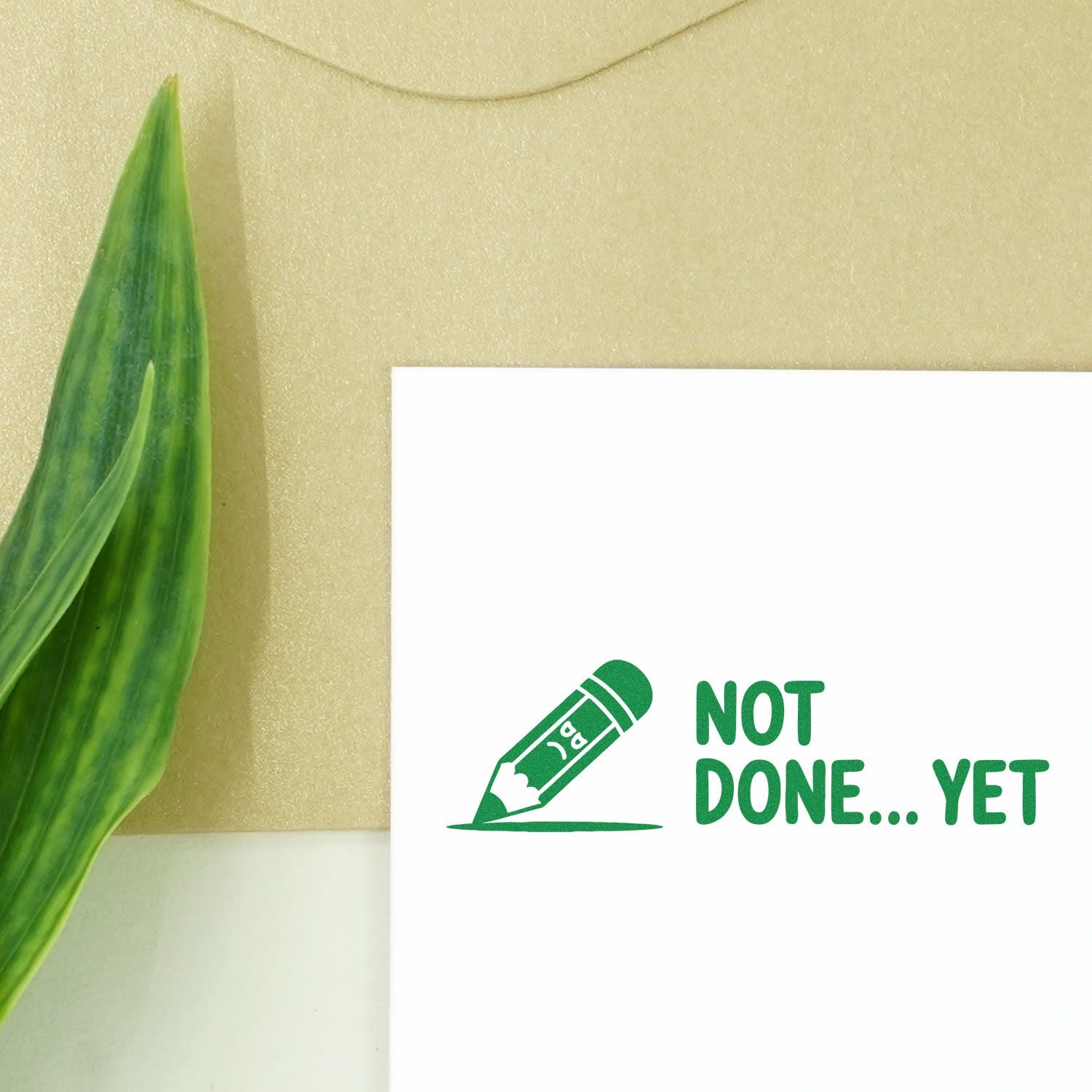 Green stamp and seal reading NOT DONE... YET with pencil icon on white paper, beside a green leaf on a beige background.