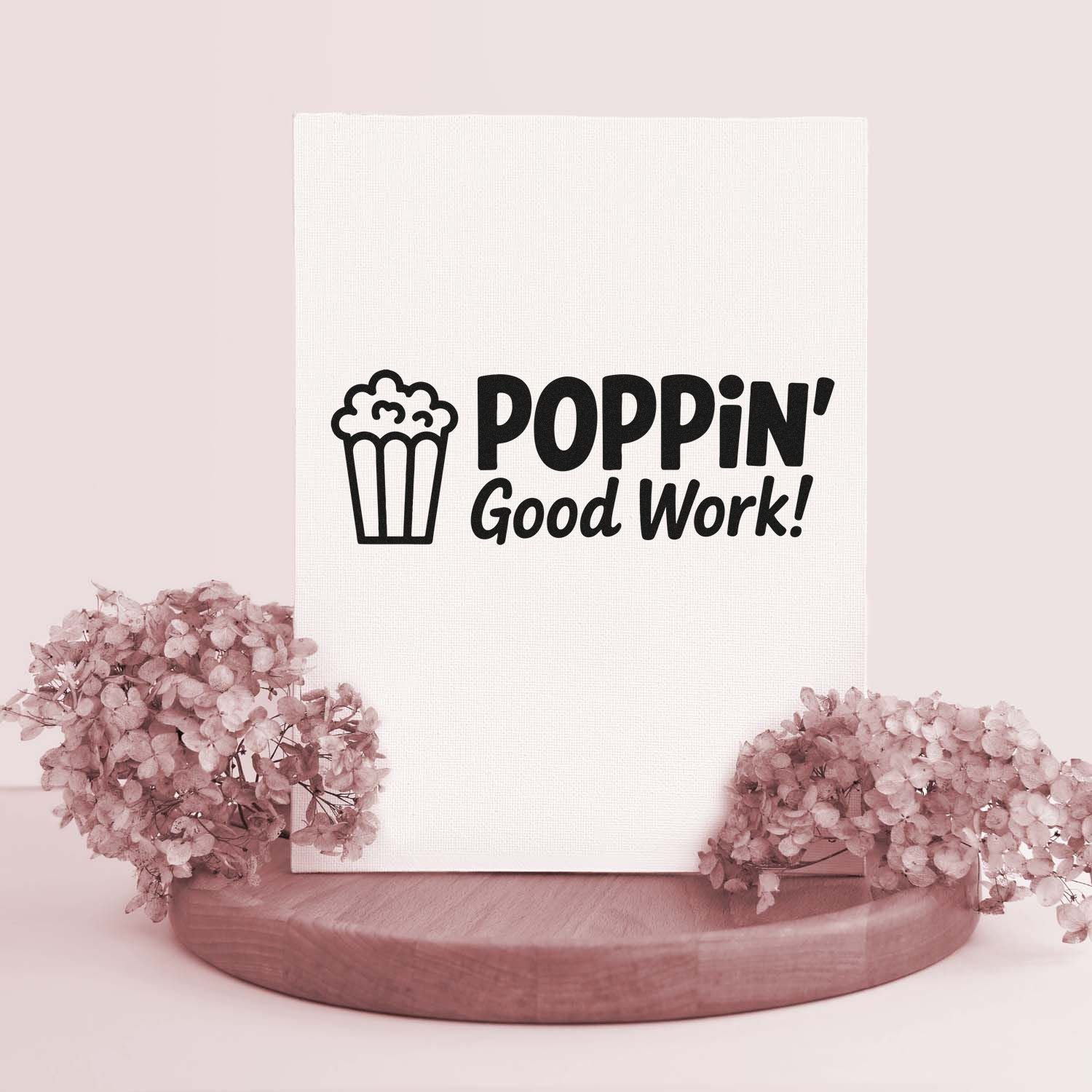 Black popcorn stamp seal reading POPPIN Good Work! on white canvas, styled with blush pink flowers and wood base.
