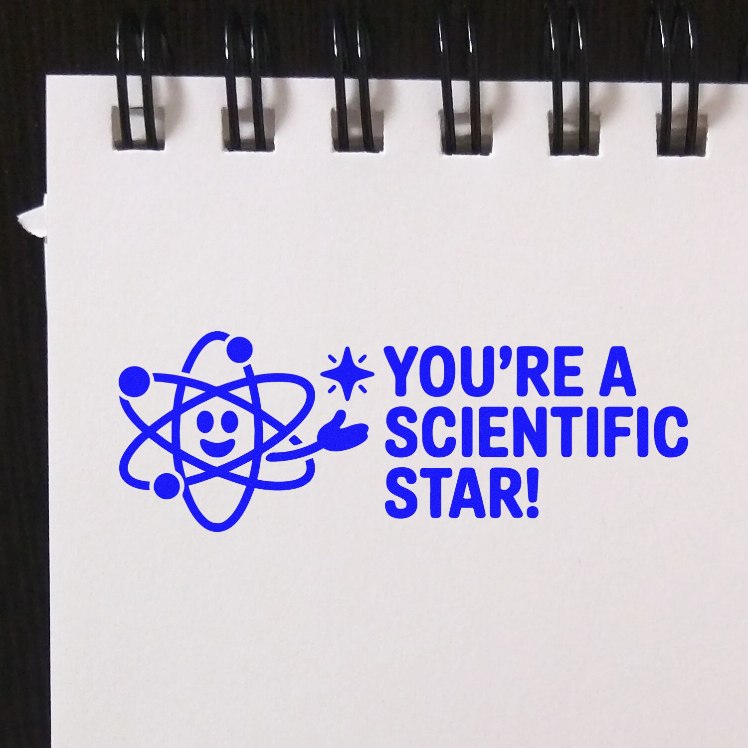 Blue stamp and seal design with a smiling atom and Youre a Scientific Star! in bright blue on white paper.