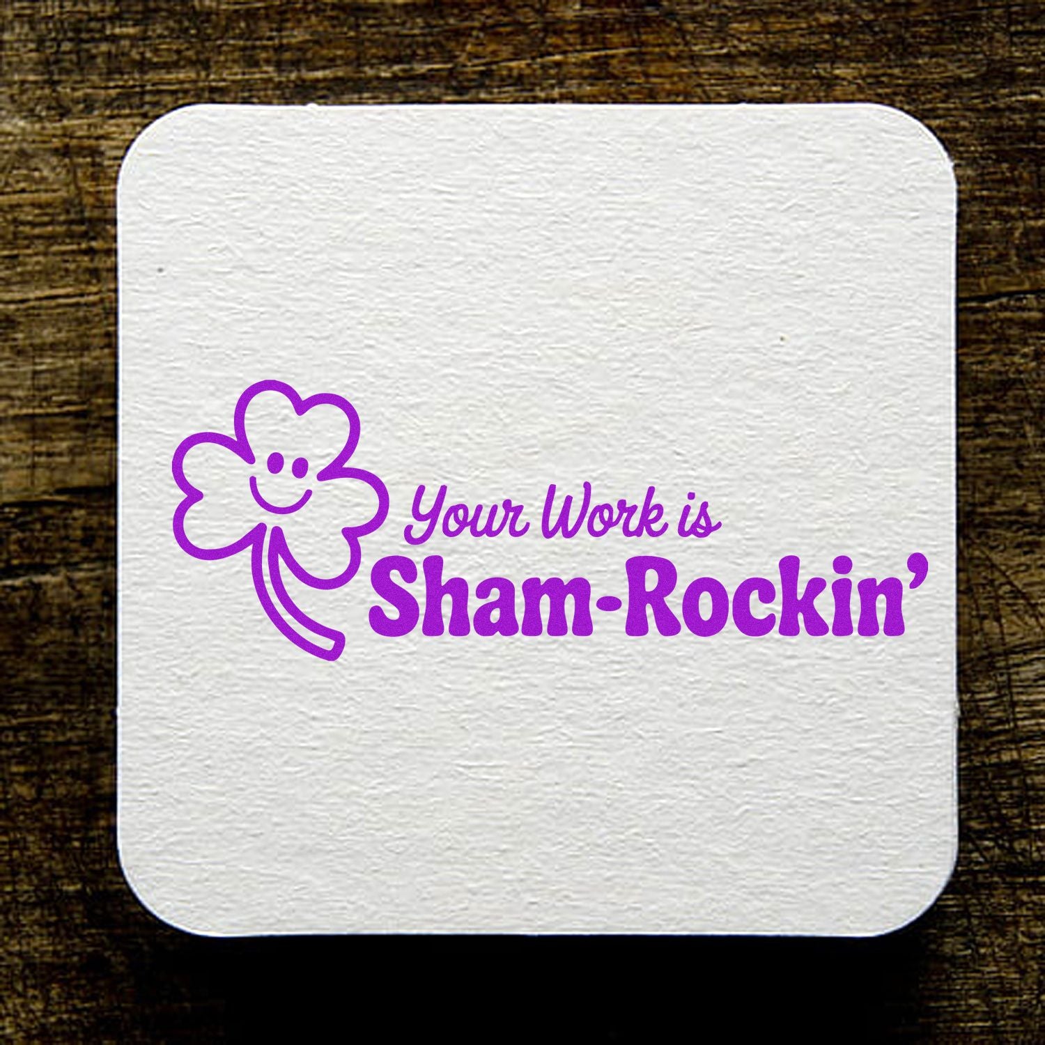 White textured square stamp/seal with purple shamrock smiley and Your Work is Sham-Rockin on a dark wood background.