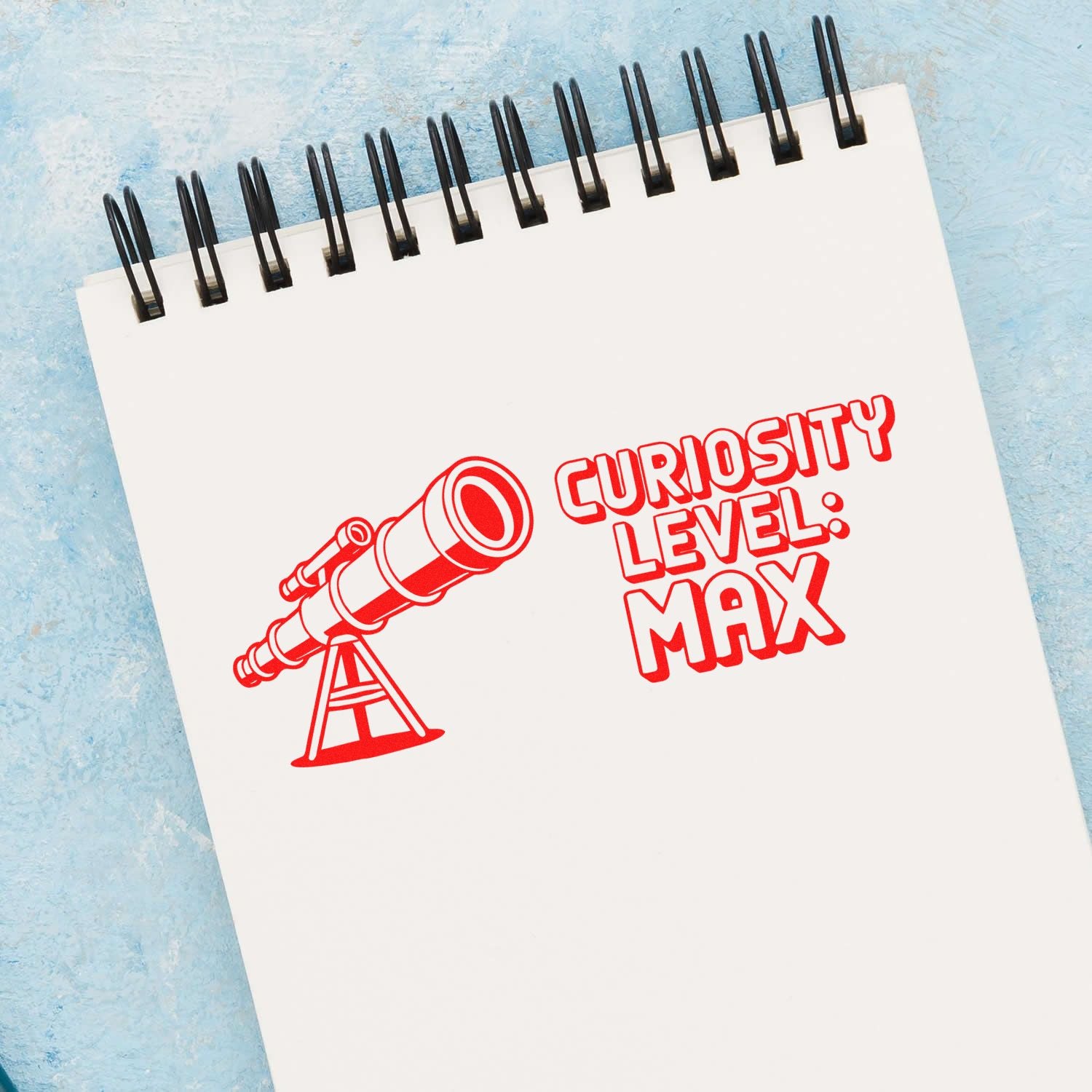 Red telescope stamp and seal on a white spiral notepad reading Curiosity Level: Max against a light blue background.