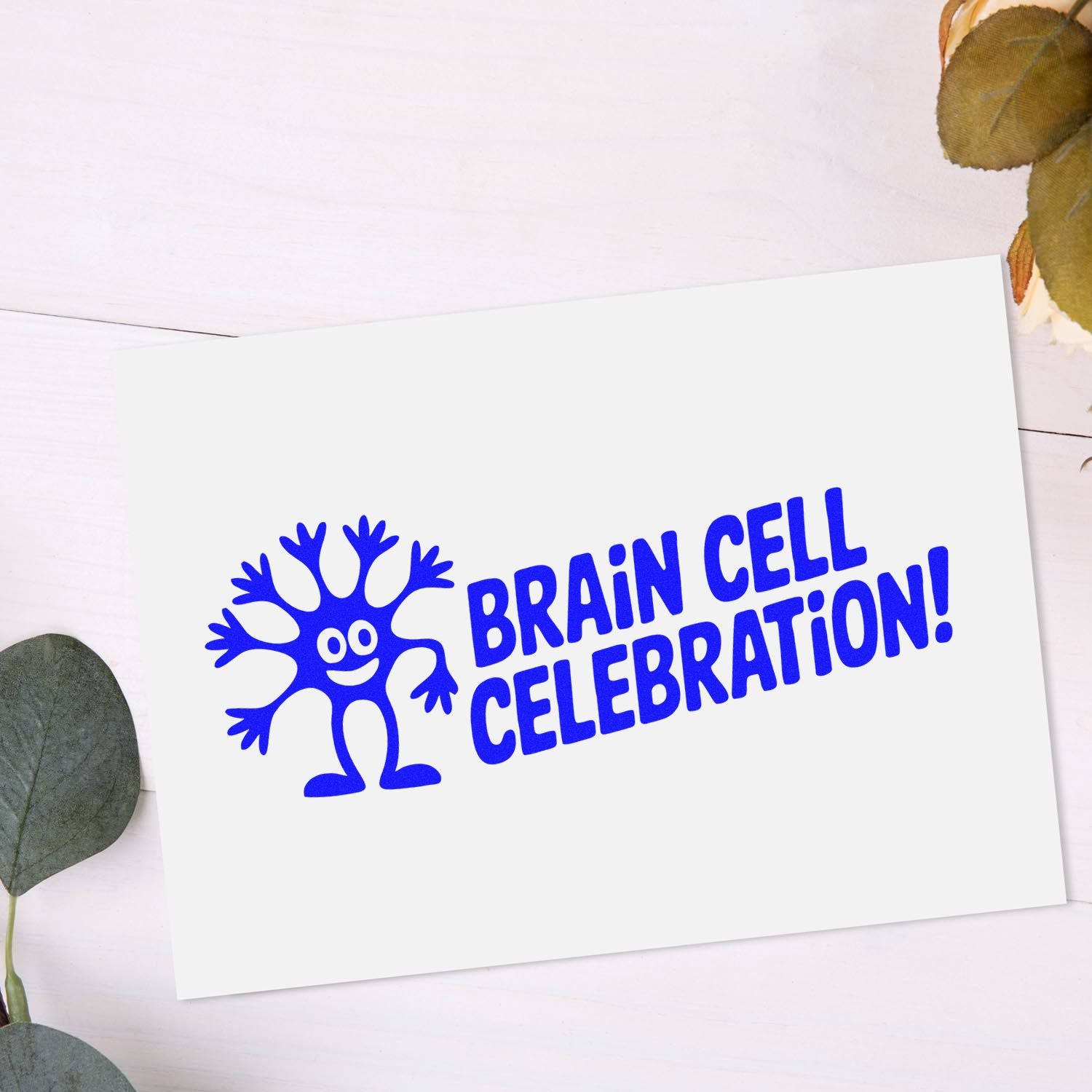 Blue Brain Cell Celebration stamp and seal on white card, featuring a playful blue character logo and leaf accents.