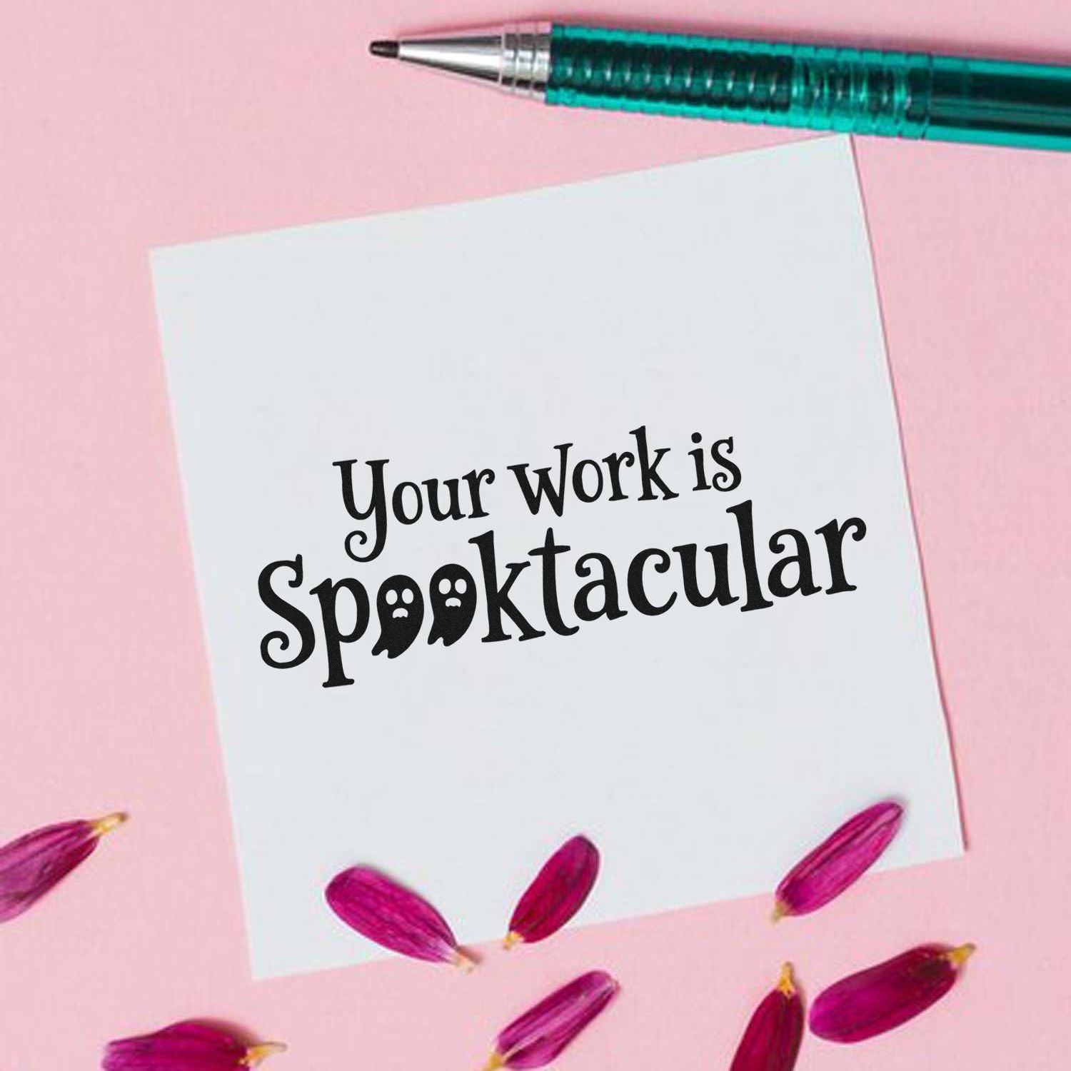 Black Your work is spooktacular stamp on a white card, with a teal pen and pink floral accents on a pastel pink background.