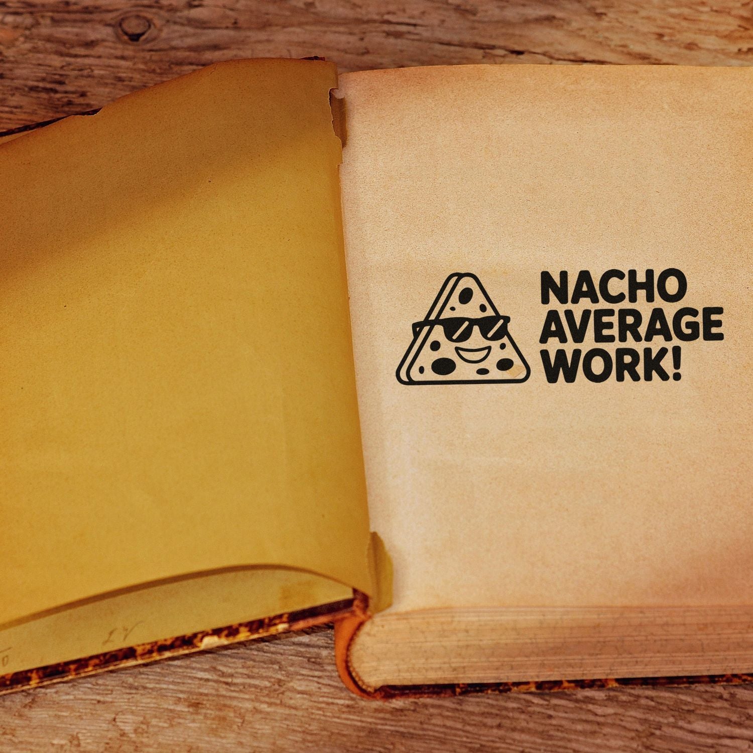 Tan notebook with a black rubber stamp seal reading Nacho Average Work! and a smiling nacho icon.