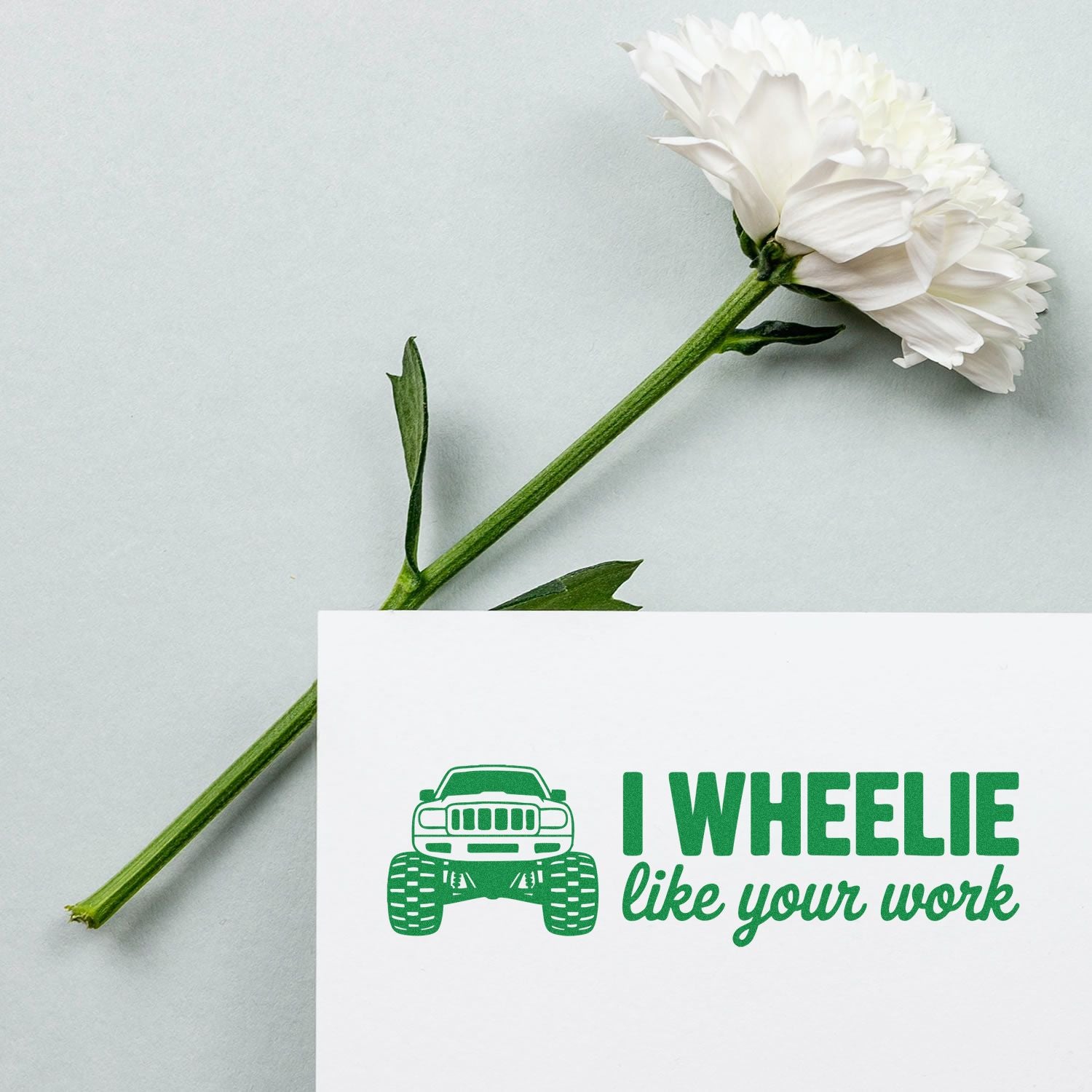 White flower beside a green rubber stamp design with truck icon and I WHEELIE like your work on a white card.