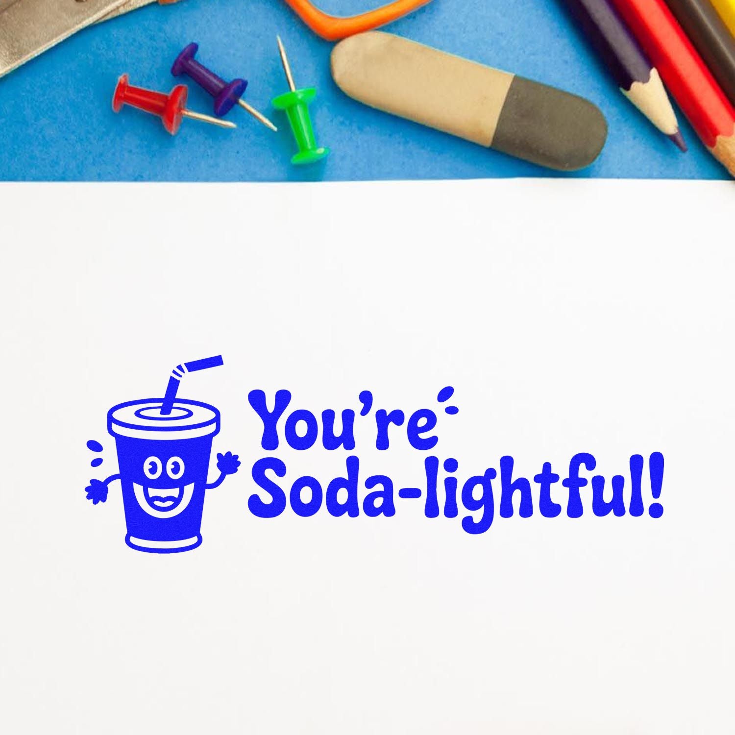 Blue custom stamp and seal design with smiling soda cup and Youre Soda-lightful! on white, with pencils and pins above.