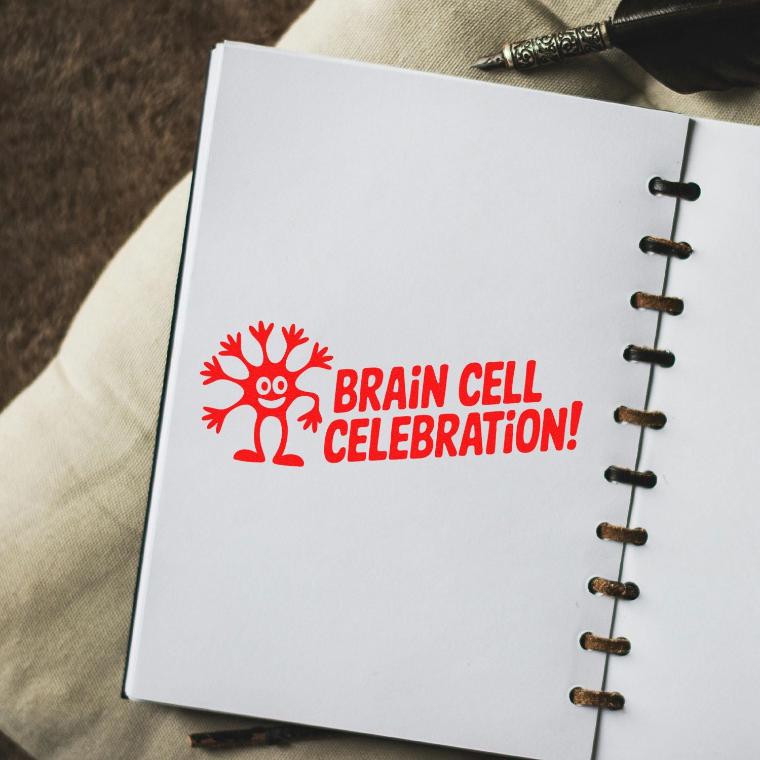 Red Brain Cell Celebration! stamp seal on white notebook page with spiral binding and black pen.