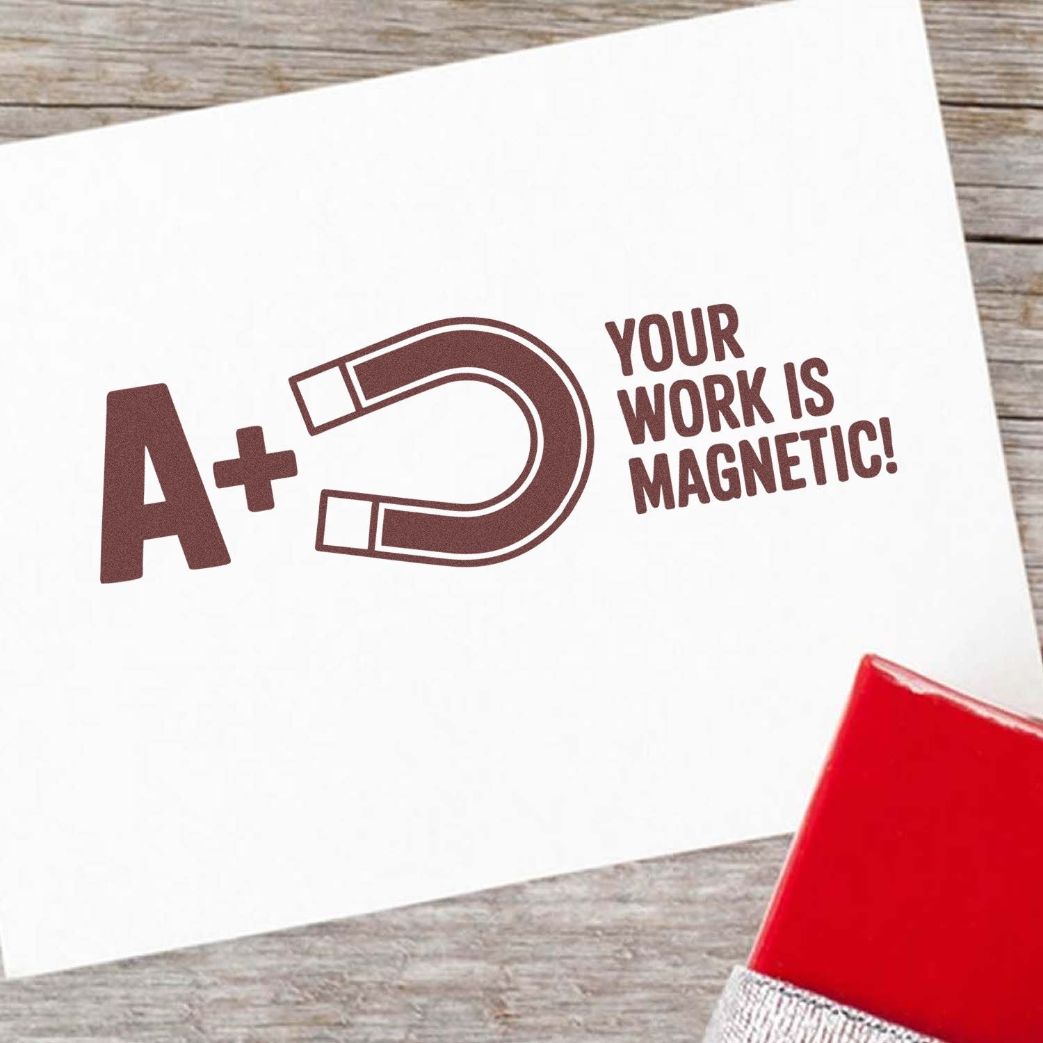 Brown A+ magnet-themed stamp and seal on white paper, with red stamp block and Your work is magnetic! text.