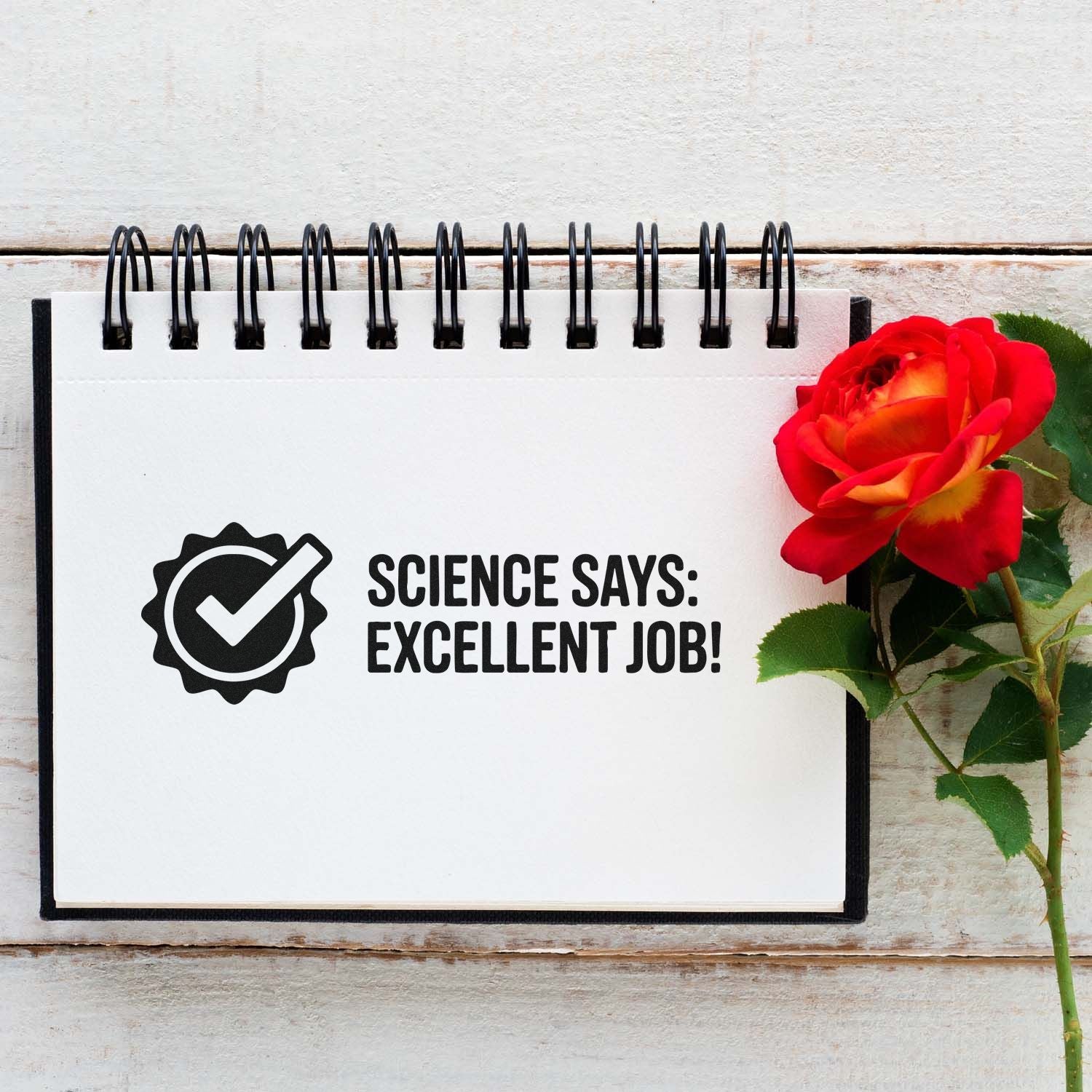 Black stamp-and-seal design on white spiral notebook says Science Says: Excellent Job! beside a red rose.