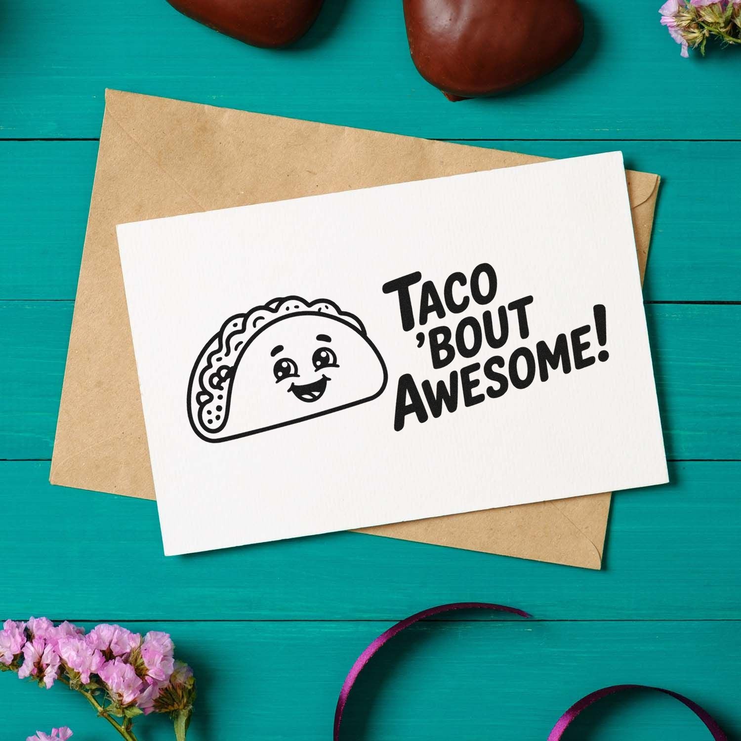 Taco-themed stamp design with black Taco bout awesome! on a white card over a brown envelope, on teal wood.