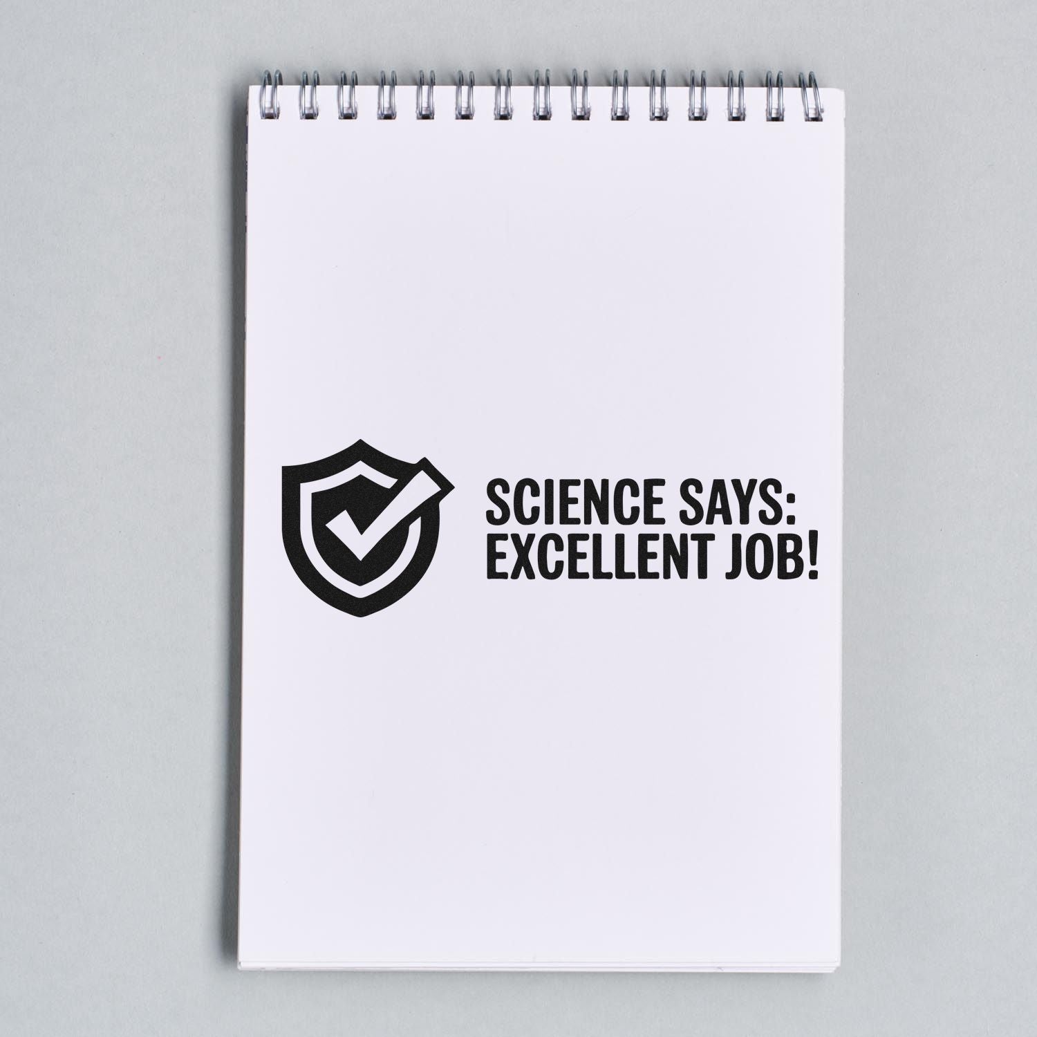 Black stamp-style approval seal with shield check and Science Says: Excellent Job! on white spiral notepad.