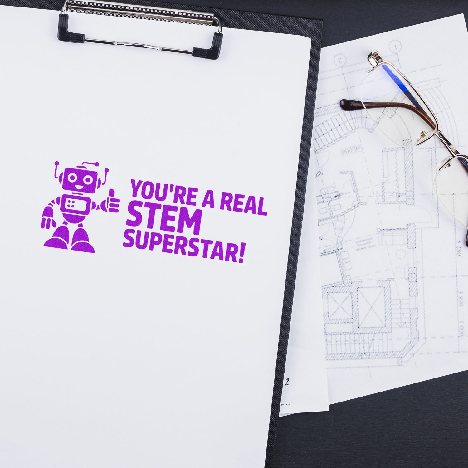 Purple STEM Superstar stamp seal on white clipboard beside eyeglasses and a blueprint