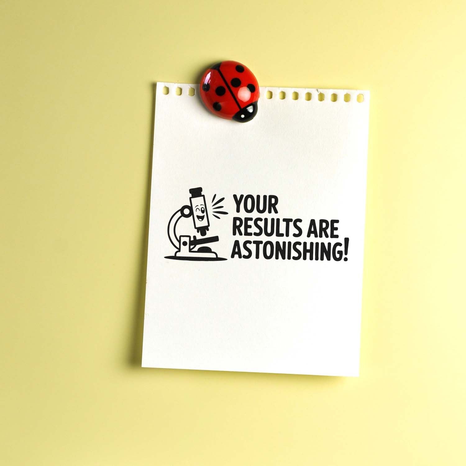 White note paper with black microscope stamp reading Your results are astonishing! and red ladybug seal on a yellow background.